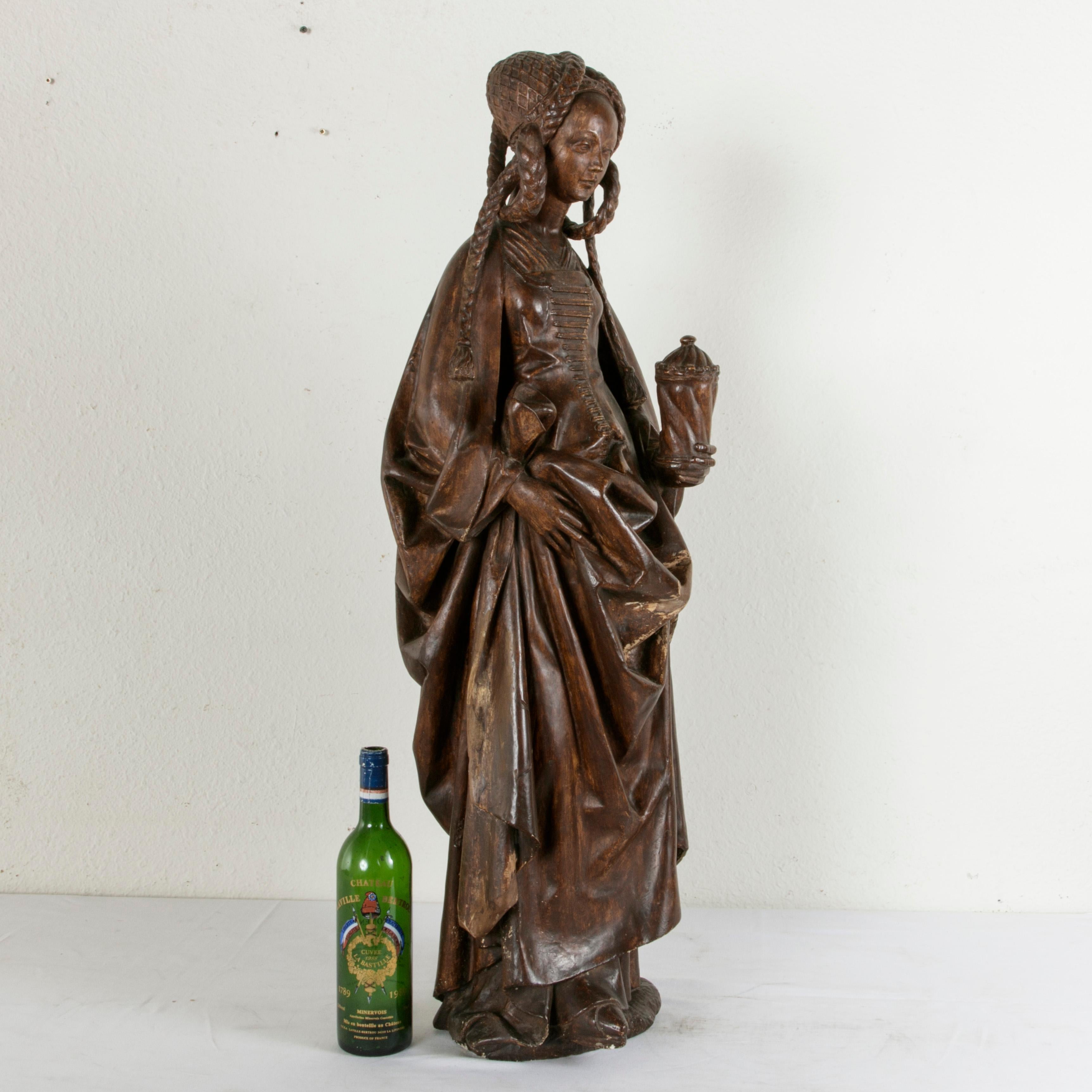 This large mid-19th century French patinated plaster over wood sculpture of Mary Magdalene features the saint clothed in fine Renaissance dress. She holds an apothecary jar of holy oil used for anointing in her left hand while her right hand gathers