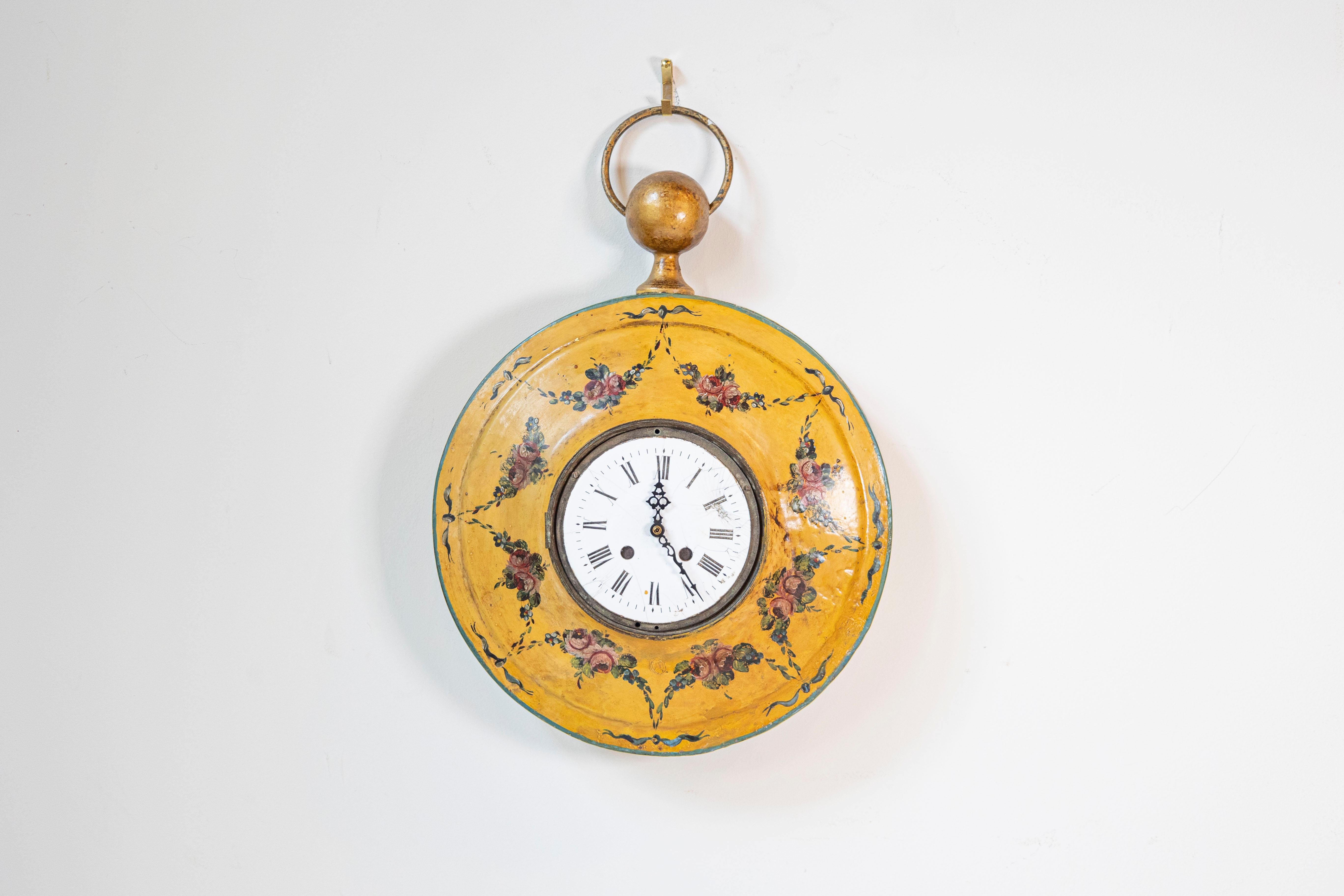 A French painted tôle pocket watch shaped wall-hanging clock with hand-painted floral décor from the early 19th century. This exquisite petite French wall clock is charmingly shaped like a pocket watch with a typical gilded circular bow at the top,