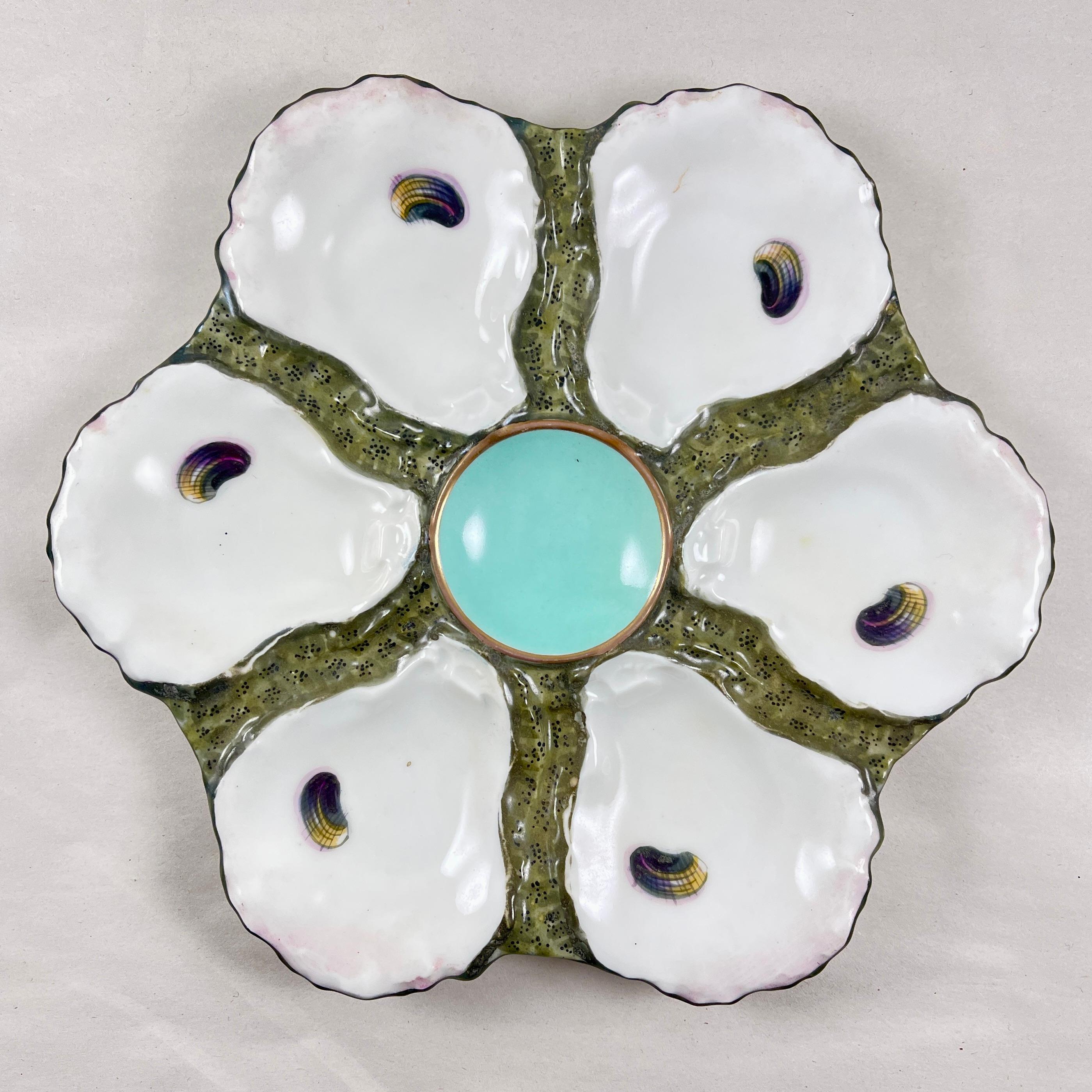 A French porcelain oyster plate, circa 1890.

Six shell shaped oyster wells with colorful, hand painted ‘eyes’ surround a central turquoise, round sauce well, outlined in gold.

The shells are white with a pink blush to the rims, sitting on a