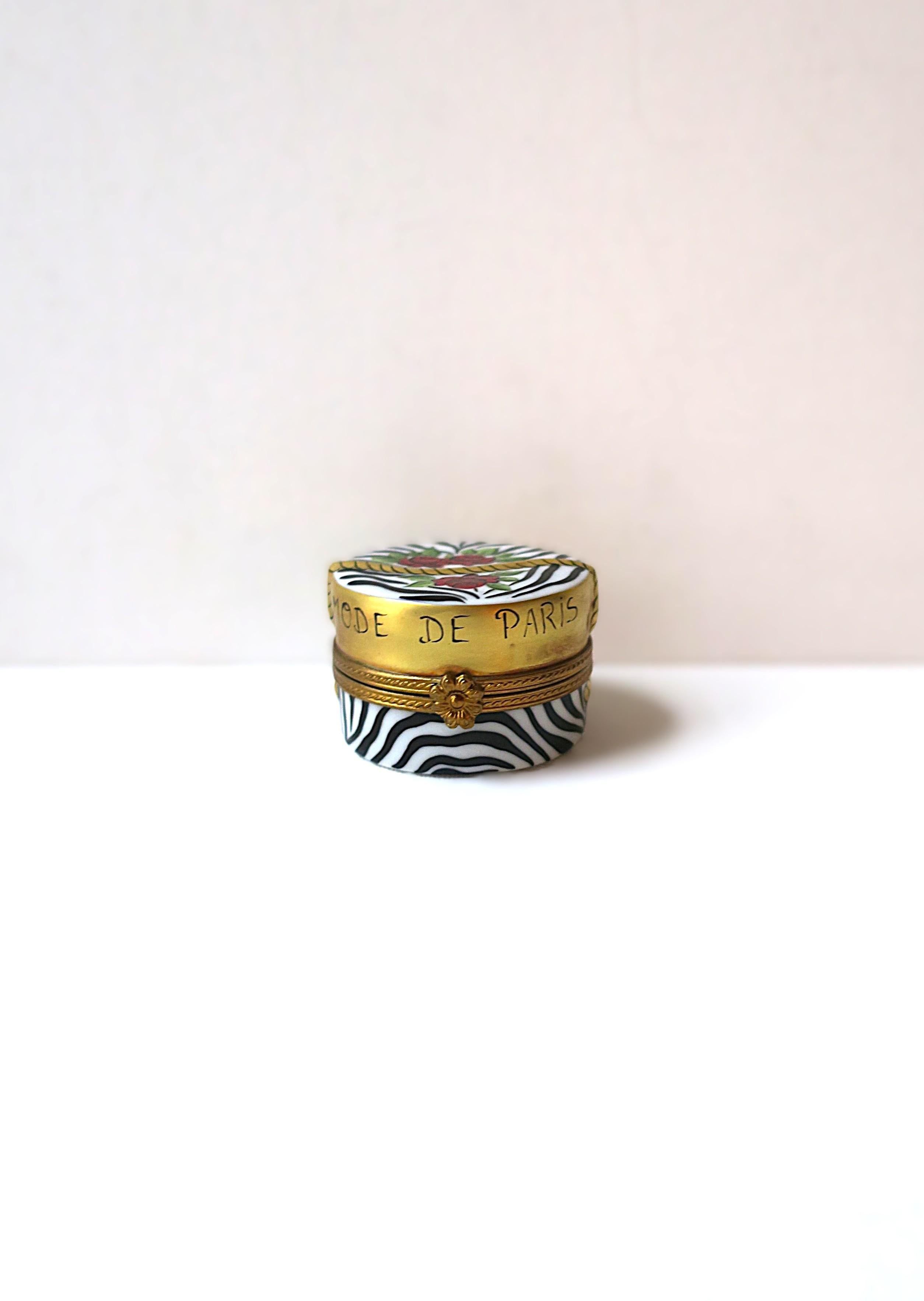 A beautiful French porcelain jewelry box 'hat box' with zebra design, circa late-20th century, France. Box is hand-painted with a gold gilt lid with a rope/tassel and flower rose design, featured across front and back reads 'Mode de Paris' aka