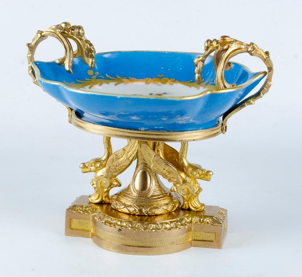 France, mid-19th century, Sevres, gilt bronze base, two stylized swans, carrying a leaf-shaped porcelain bowl, stylized leaf handles on the sides, painting of a cupid on the mirror, sky blue background and rim.
Measures:
Height: 13