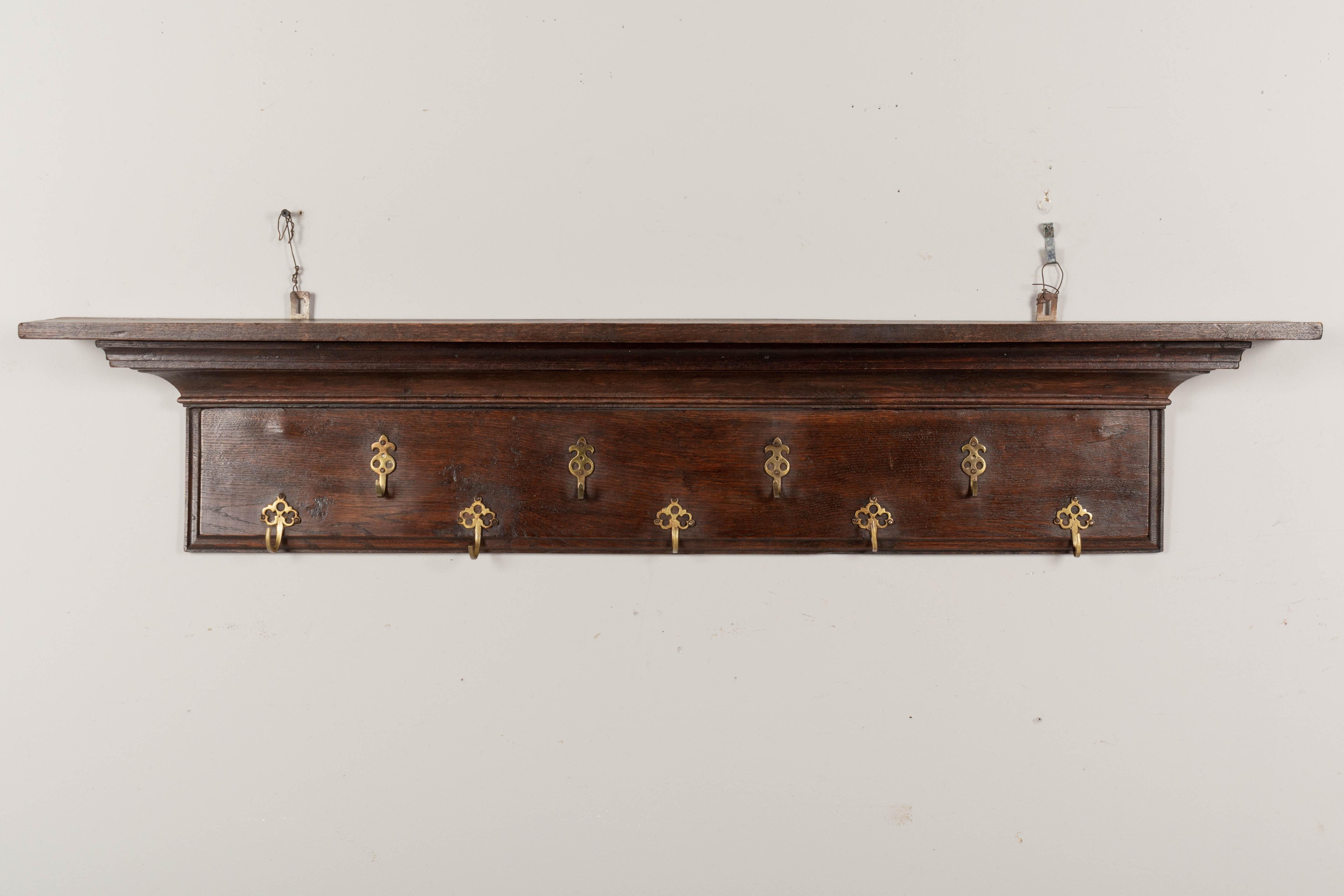 A French oak potière, or shelf with nine brass hooks for hanging pots and pans in the kitchen. The top ledge has two grooves to display plates and platters.