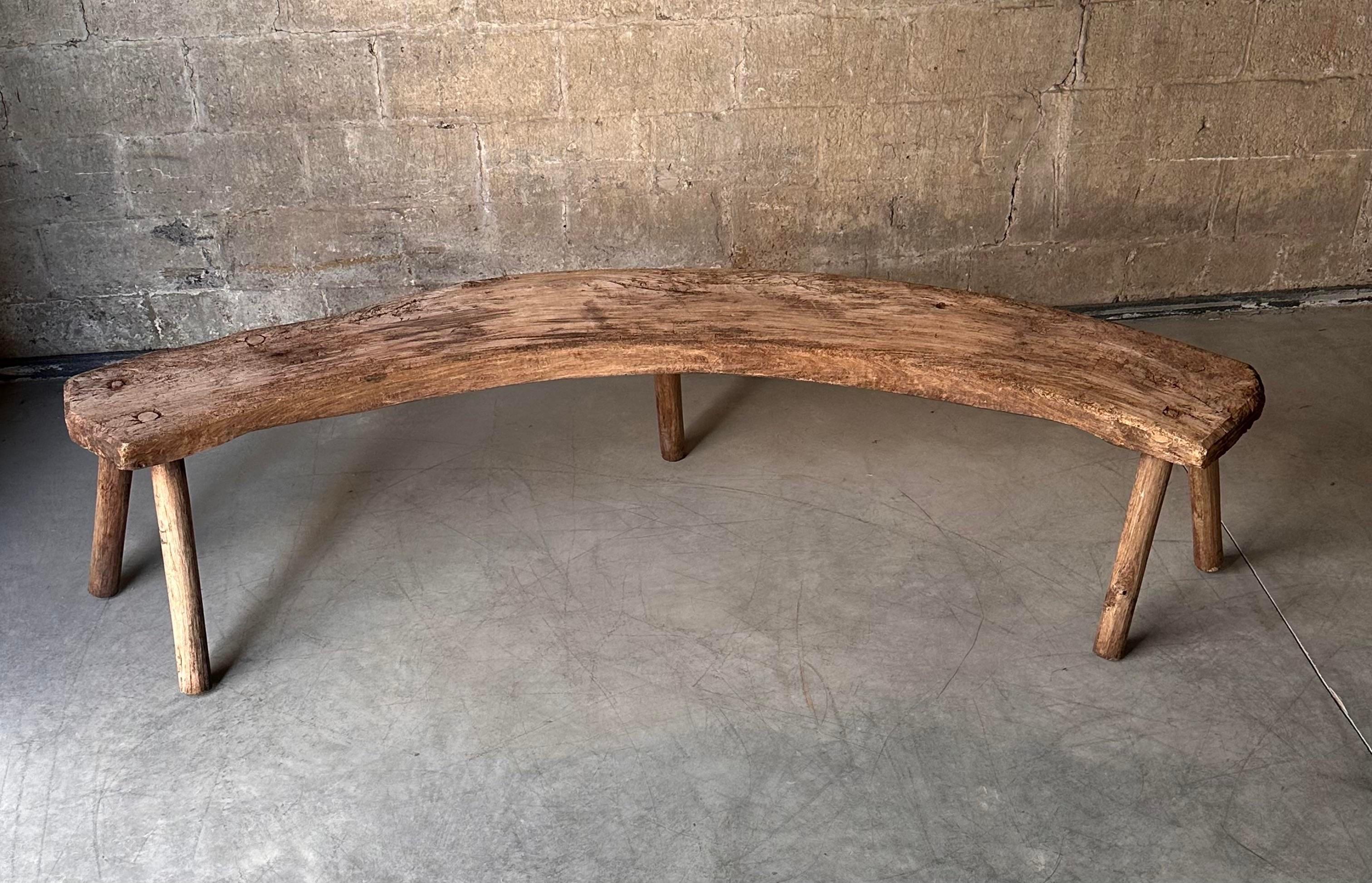 A charming French antique bench. Primitive in style and long with a gentle curve, it stands on five round straight legs. Such a unique shape!