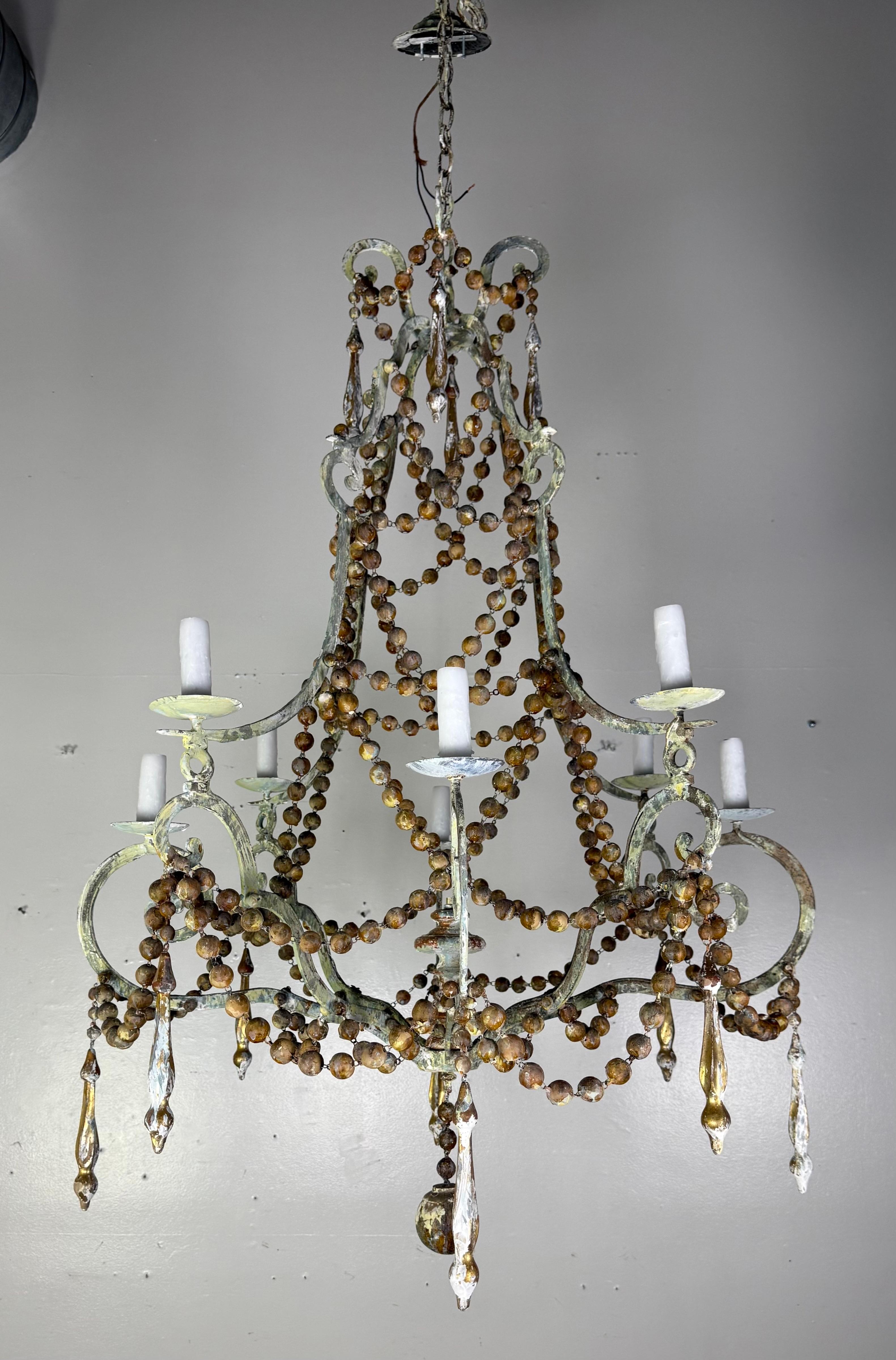 Sorprendente ejemplo de la elegancia rústica provenzal francesa, esta lámpara de araña capta el encanto del campo con su bella presencia envejecida. Fabricada con una estructura de hierro pintado, está envuelta en cascadas de cuentas de madera