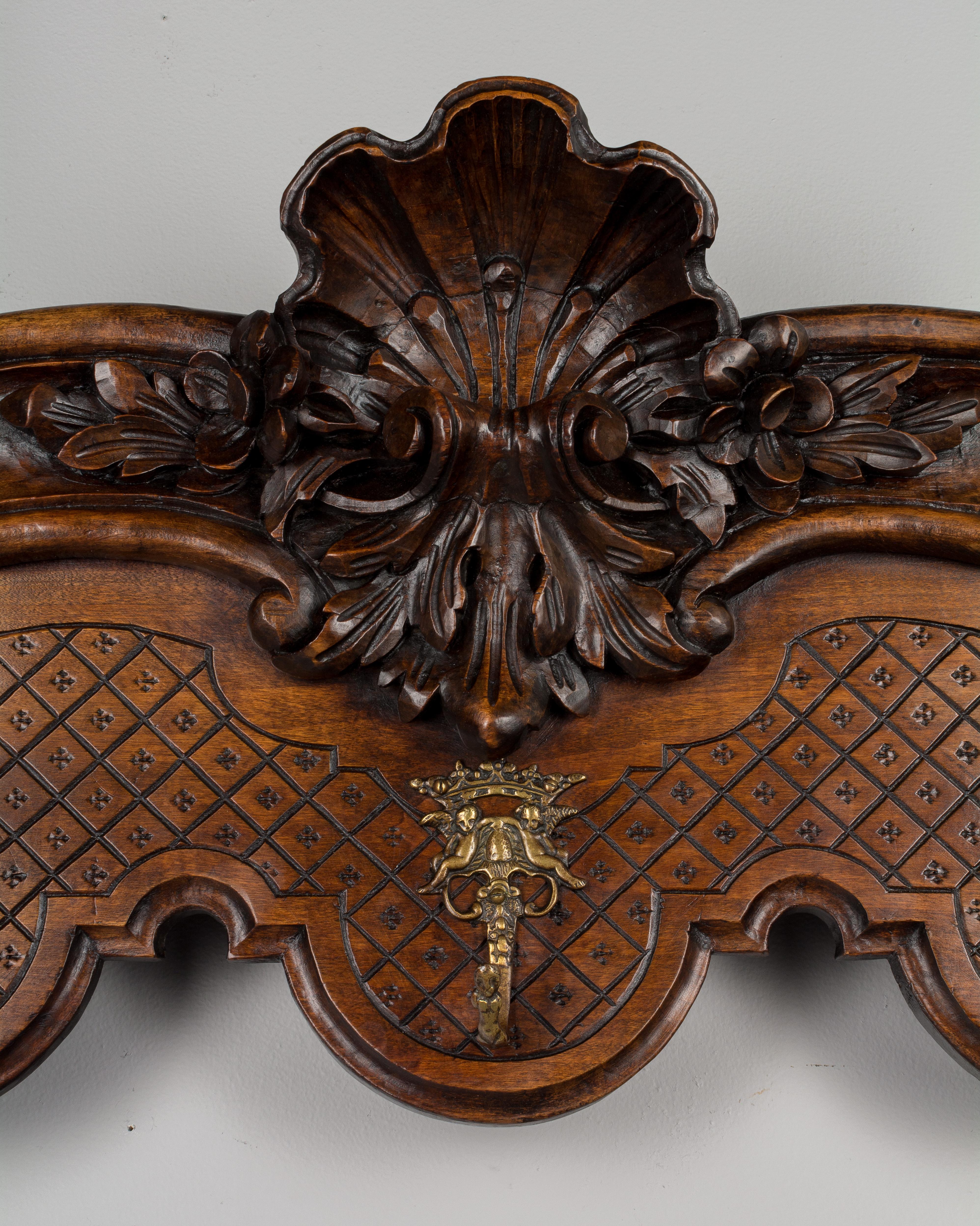 An early 20th century French Provençal potière, or shelf with brass hooks for hanging pots and pans in the kitchen. Made of solid walnut with bold, hand-carved decoration including a large shell form with flowers in the center and at the corners.