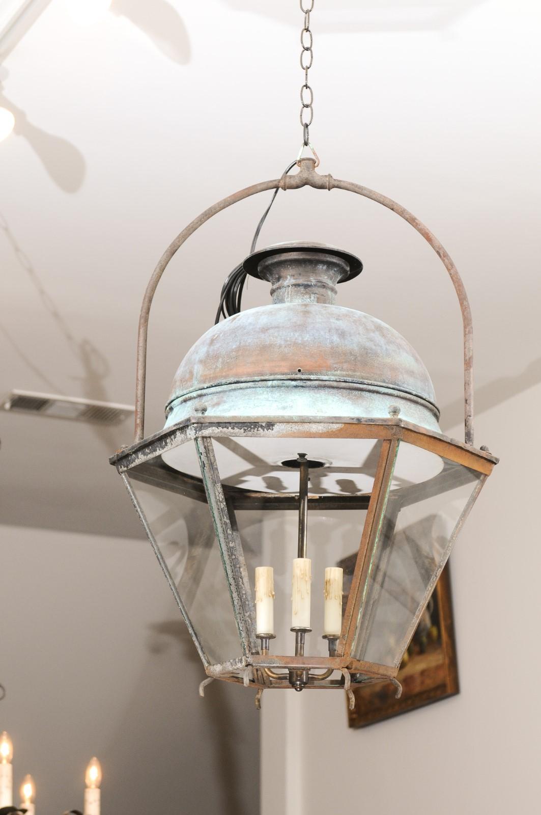 A French Provençal copper and iron hexagonal lantern from the early 20th century, with three lights and glass panels. Created in Southern France at the Turn of the Century, this lantern features a copper dome with verdigris patina, sitting above an