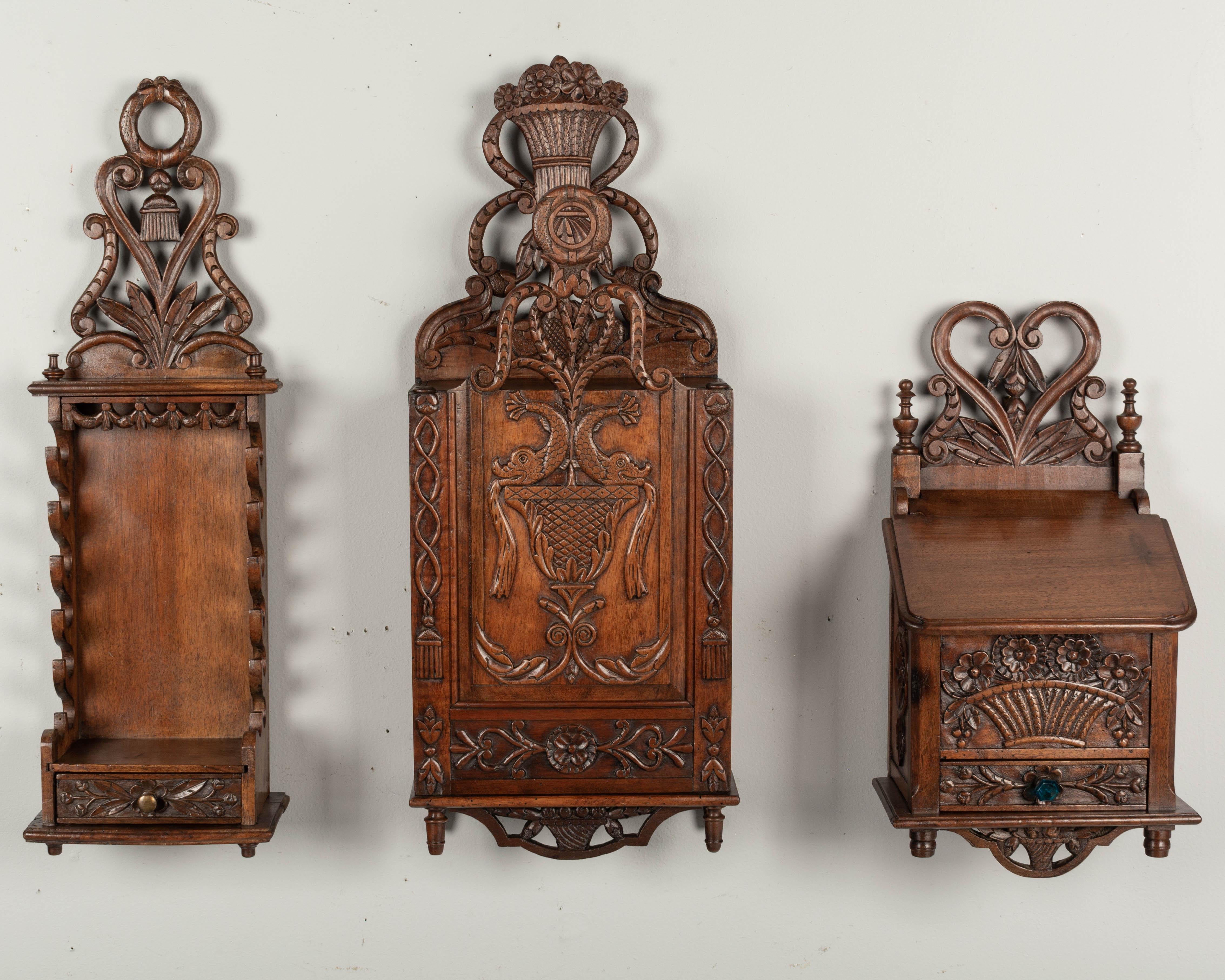 A set of three early 20th century French Provencal decorative boxes including a a porte couteaux, or knife rack, a fariniere, or flour box and a boite à sel, or salt box. Each made of walnut with fine hand-carved decoration and elaborate pierced