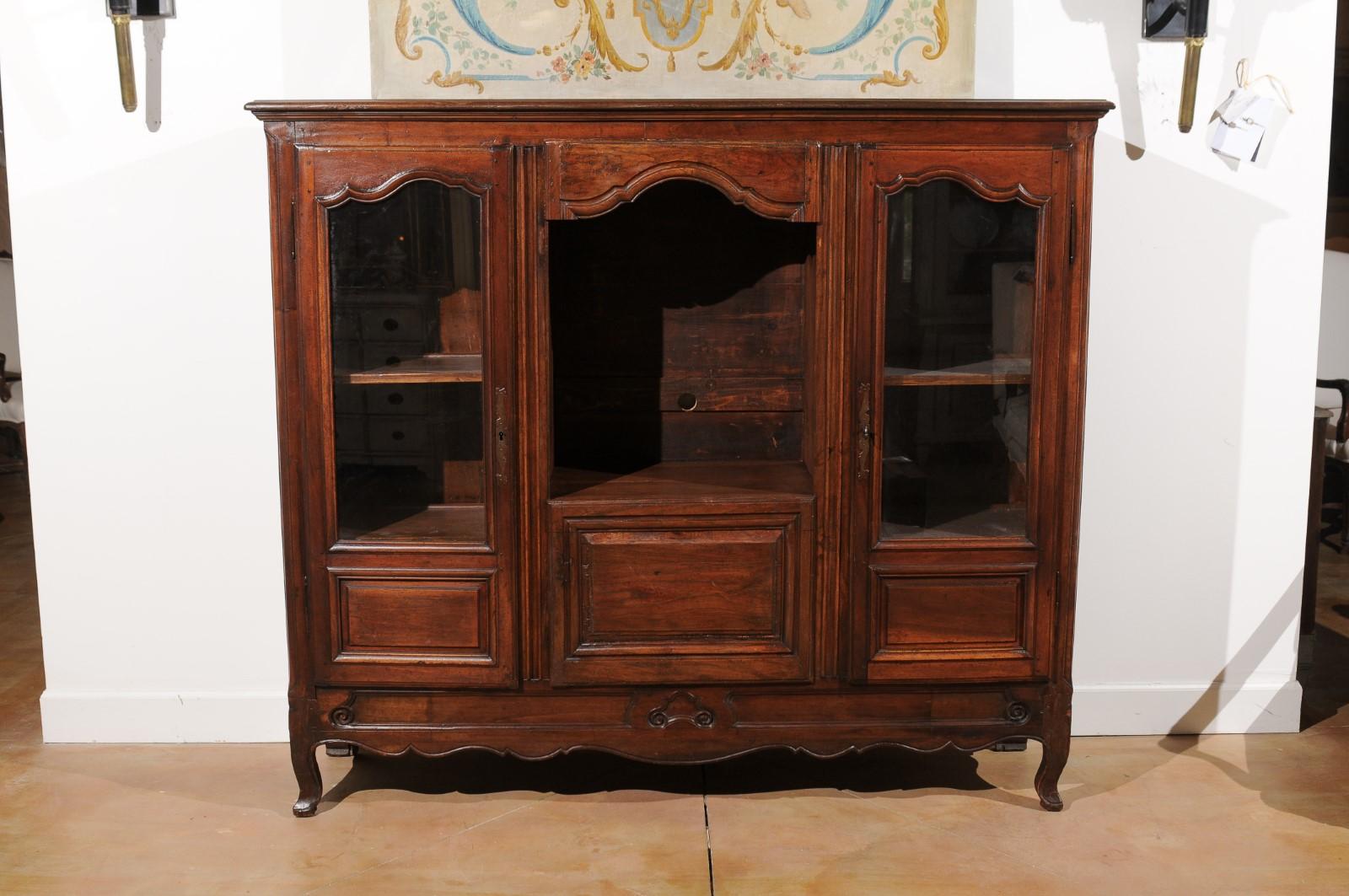 A French Provincial walnut bibliothèque from the late 18th century, with glass doors and open shelf. Created in France during the last quarter of the 18th century, this walnut bookcase features a perfectly harmonious façade made of two glass doors