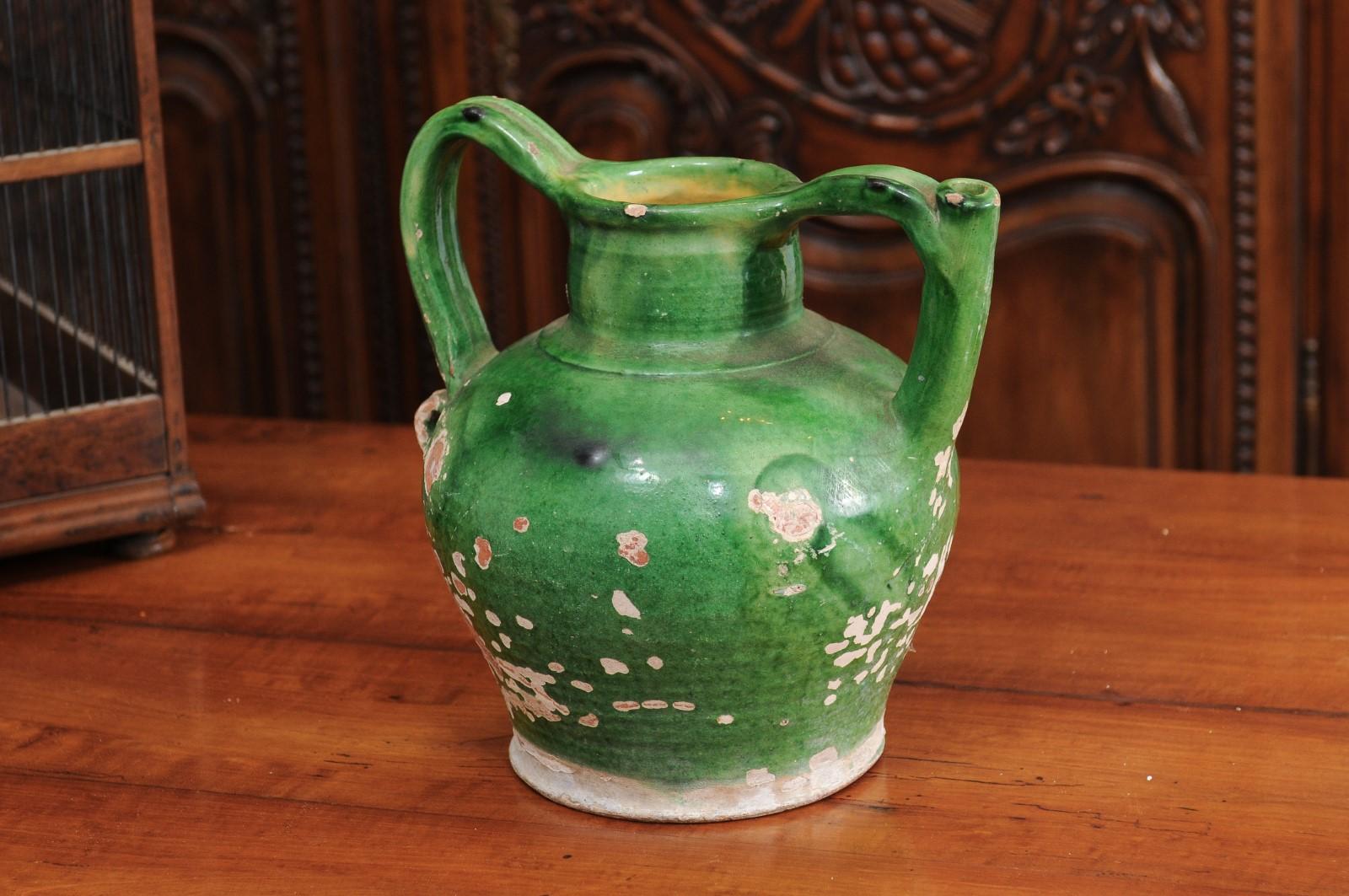 A French Provincial green glazed pottery olive oil jug from the mid-19th century, with double handles, front spout and distressed patina. Created in Southern France at the beginning of Emperor Napoleon III's reign, this jug features a green glazed