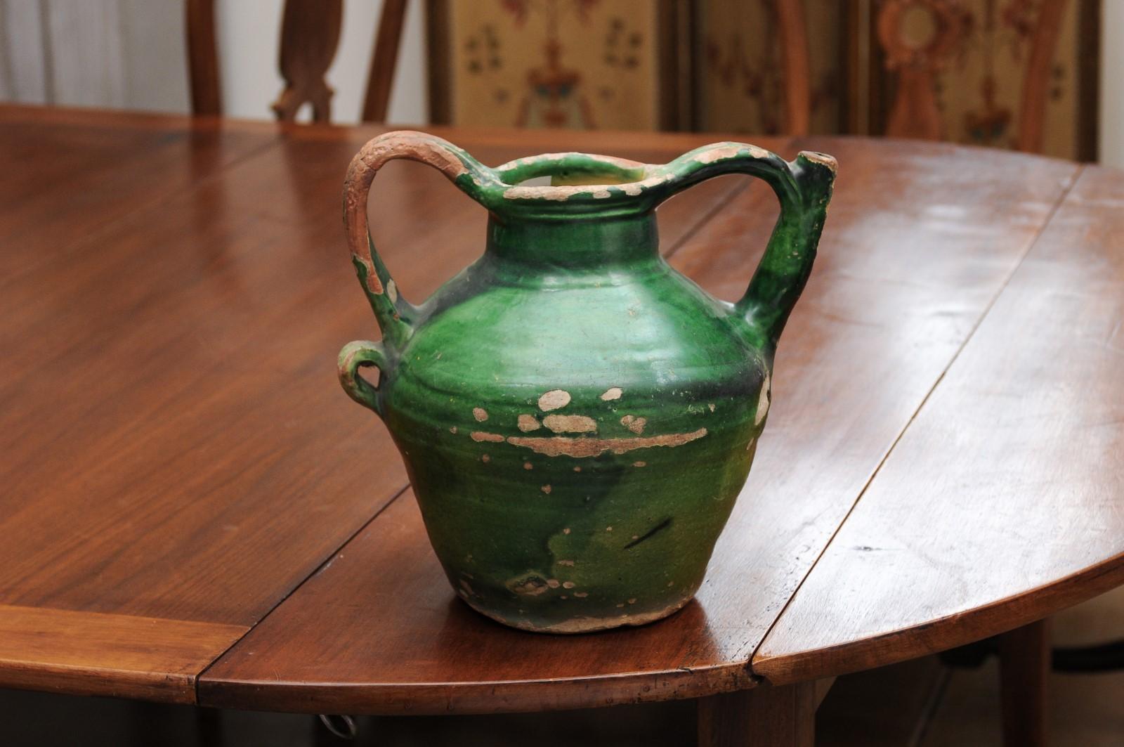 A French provincial green glazed pottery olive oil jug from the mid-19th century, with double handles, front spout and distressed patina. Created in Southern France at the beginning of Emperor Napoleon III's reign, this jug features a green glazed
