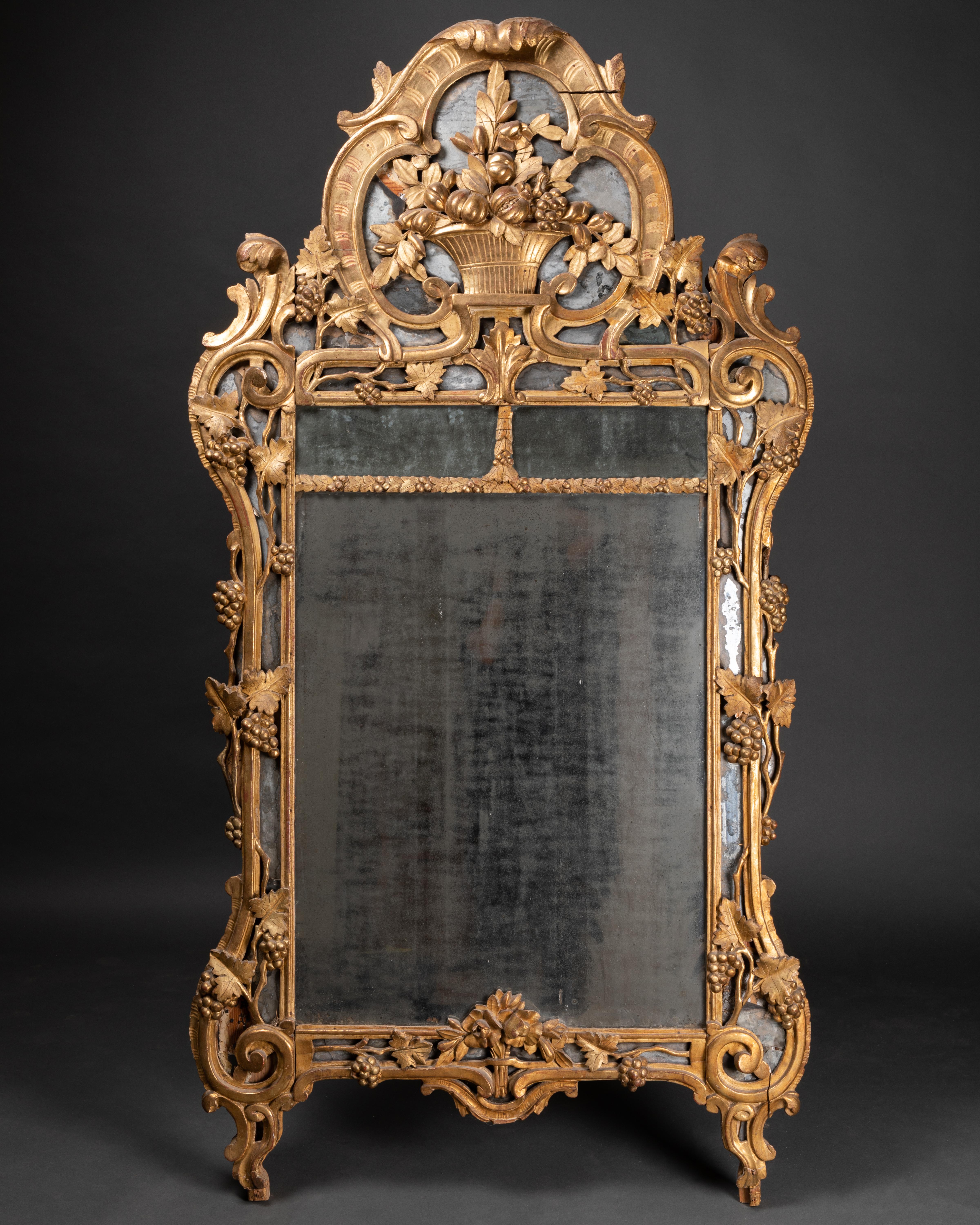 French provincial work from the 18th century. Mercury mirror in carved, gilded wooden frame. Centered on a basket filled with fruit in a vine environment.