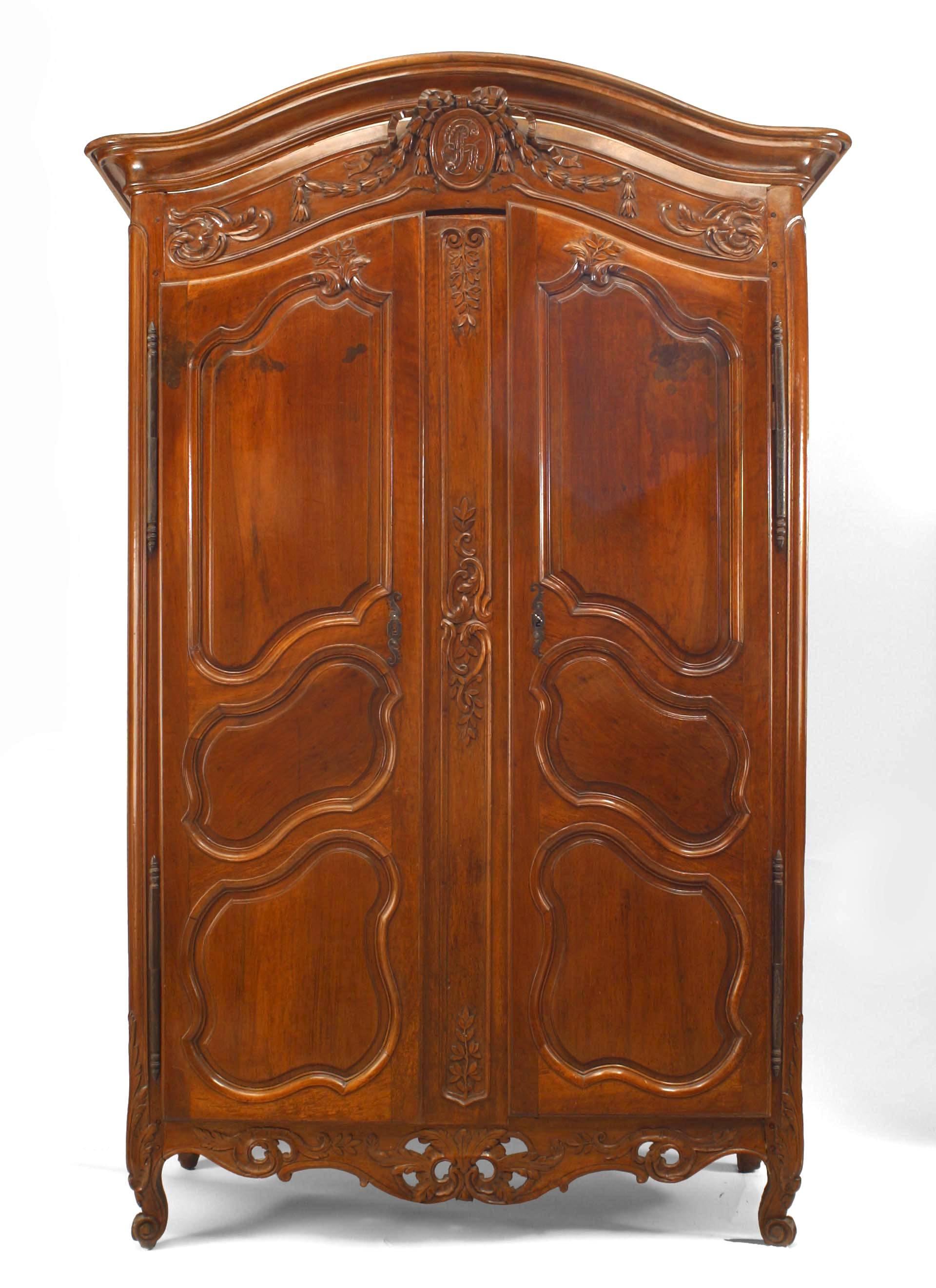 French Provincial (18th Century) walnut carved 2 door armoire with center oval medallion with initials and draped with a carved wreath and bow knot.
