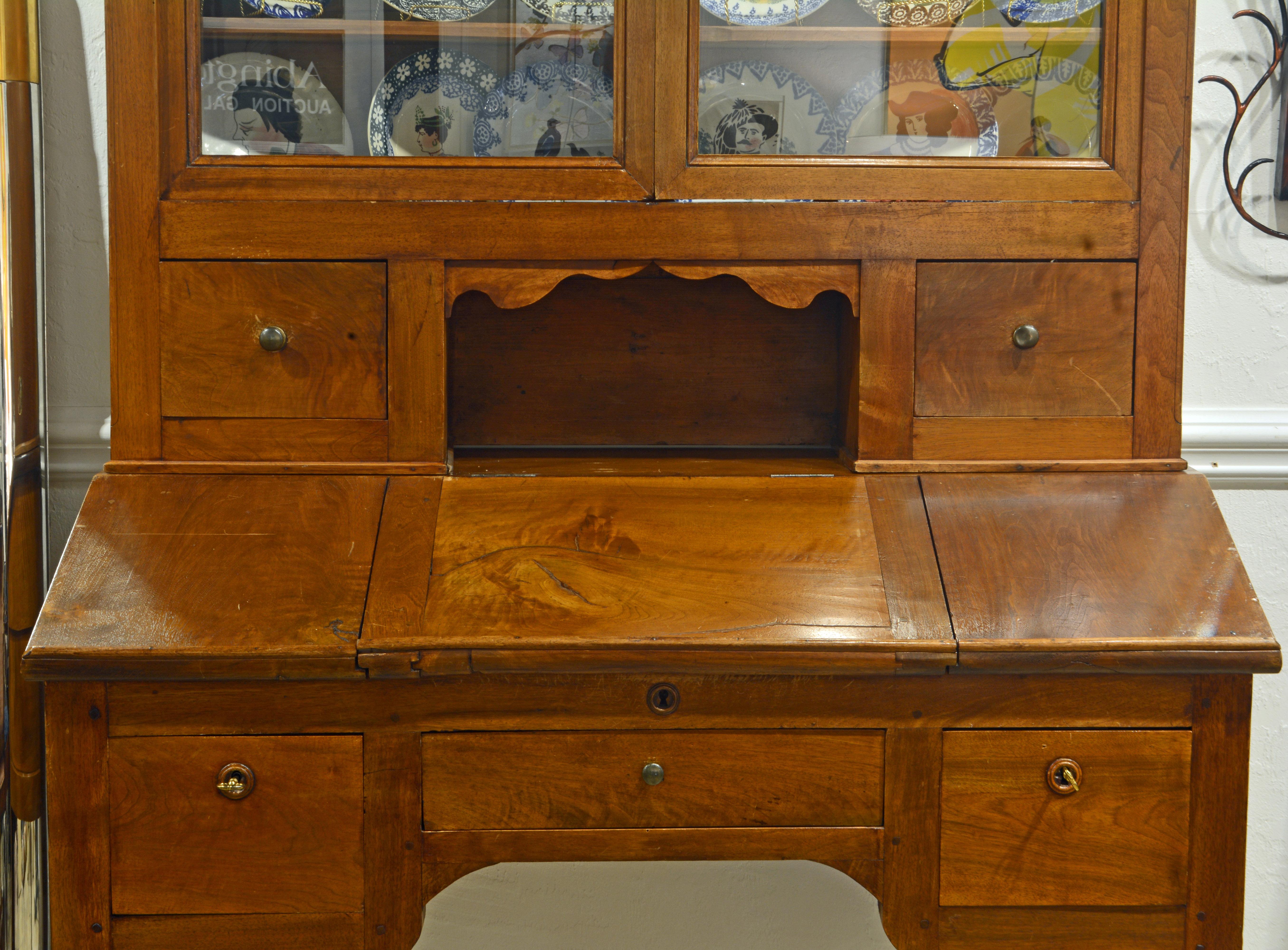 This early (circa 1830) French Provincial plantation style walnut secretary desk and bookcase features an upper part topped by a cornice above two glazed doors opening up to a shelved interior great for either books or display. An open center