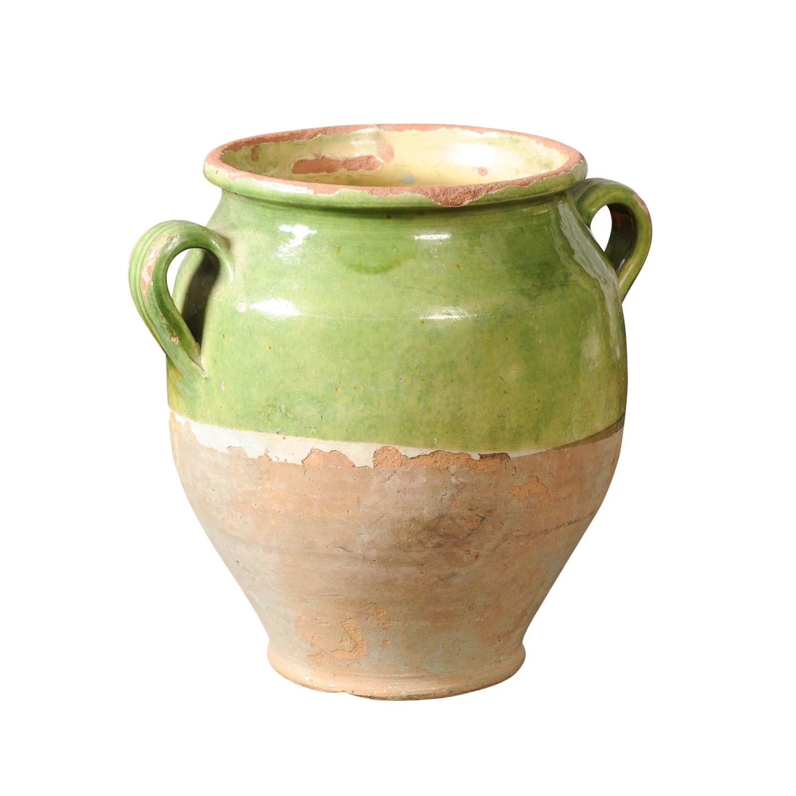 A French Provincial green glazed pot à confit from the 19th century, with two lateral handles. Steeped in rustic allure, this French Provincial pot à confit from the 19th century exudes a charm that resonates with the soul. Radiating an ethereal