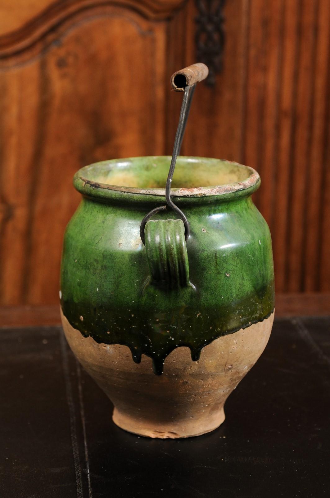 A French green glazed pottery confit pot from the 19th century with wooden handle and unglazed base. Created in France during the 19th century, this confit pot features a green glaze in its upper section sitting above an unfinished base.