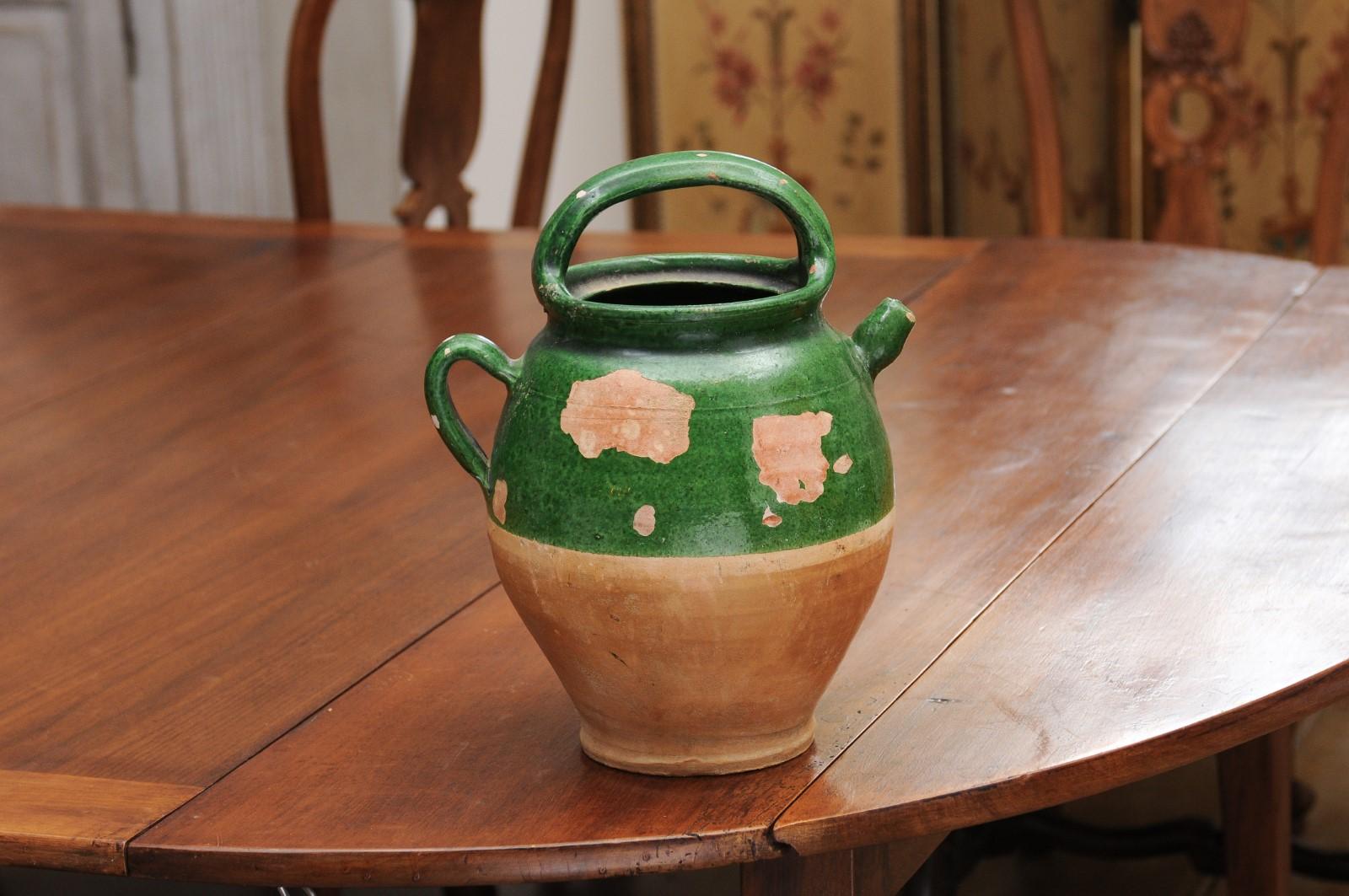 A French Provincial green glazed pottery olive oil jug from the 19th century, with two handles, front spout and distressed patina. Created in Southern France during the 19th century, this olive oil jug features a green glazed upper section perfectly