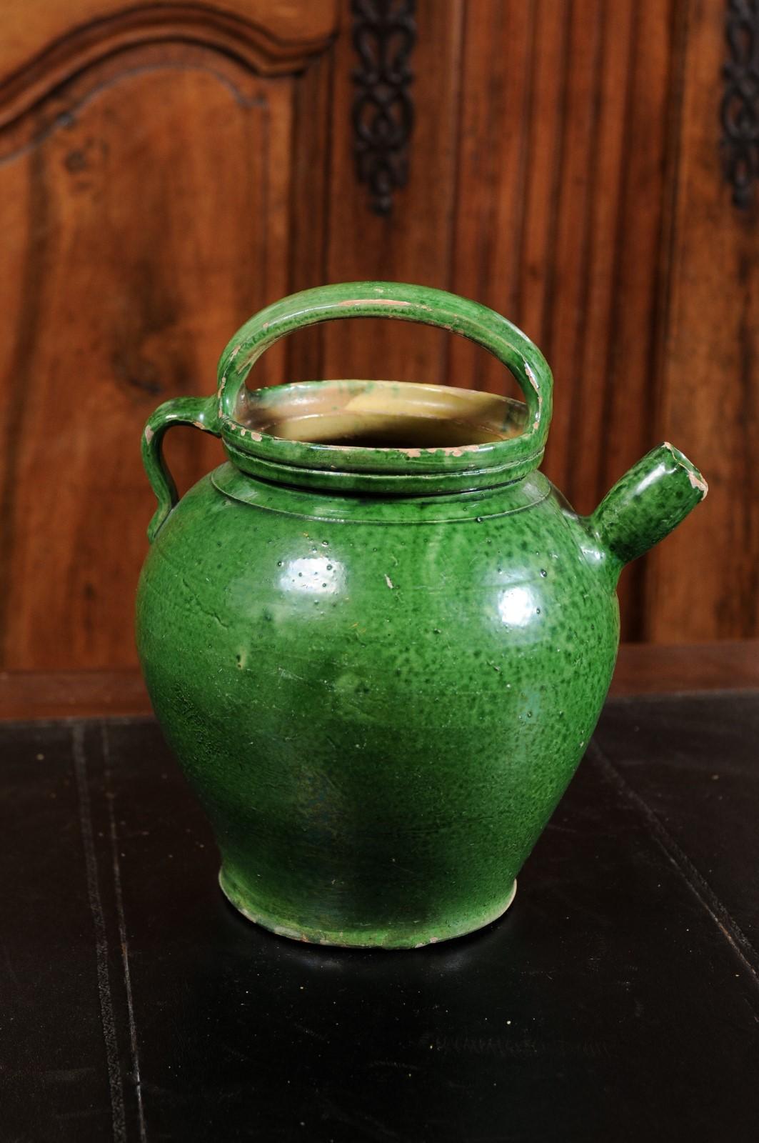 A French Provincial pottery olive oil jug from the 19th century, with green glaze, two handles and distressed patina. Created in Southern France during the 19th century, this olive oil jug features a green glazed finish perfectly complimenting its