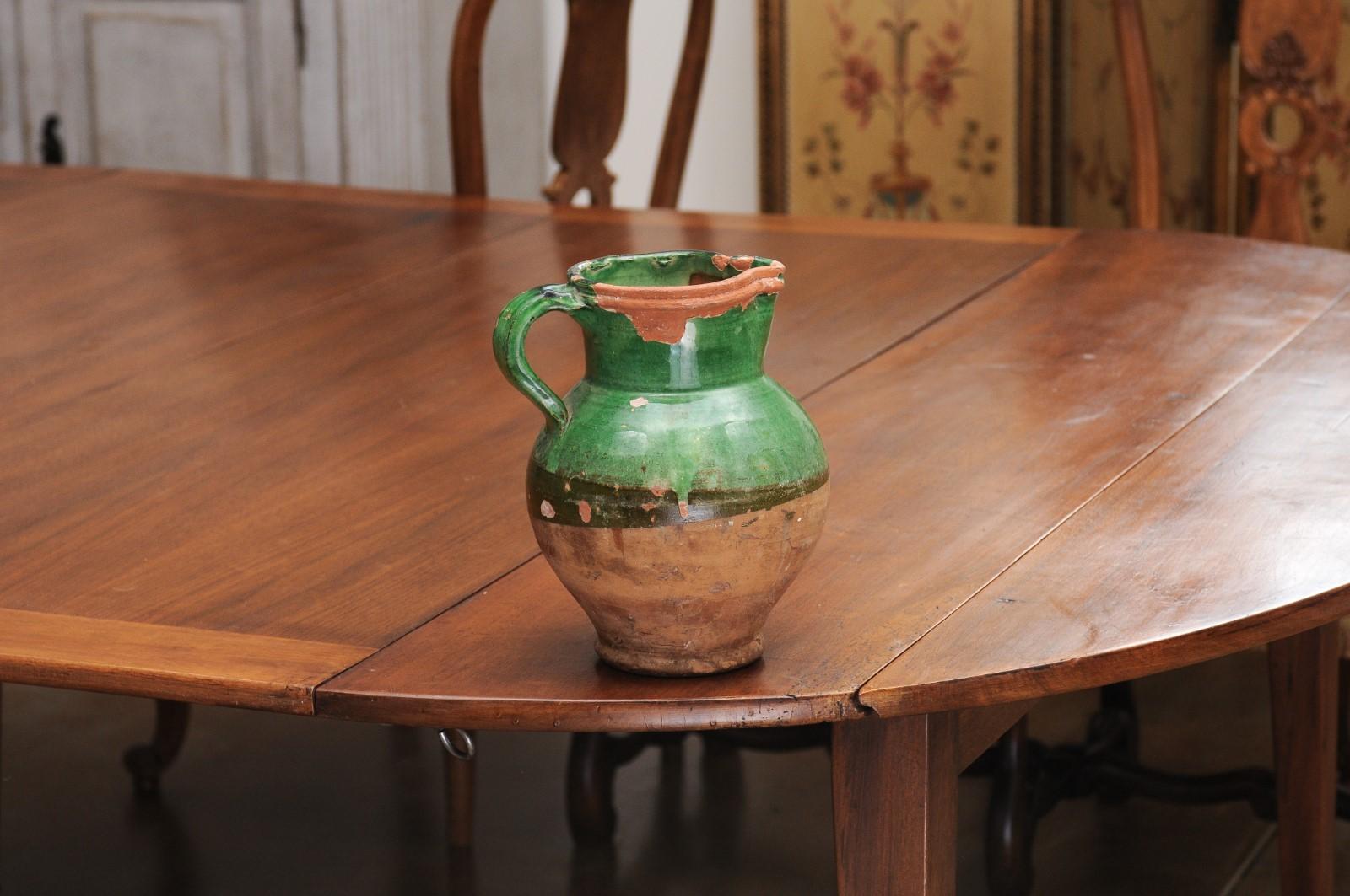 A French Provincial green glazed pottery pitcher from the 19th century, with large handle and nicely distressed patina. Created in southern France during the 19th century, this pitcher features a green glazed upper section contrasting beautifully