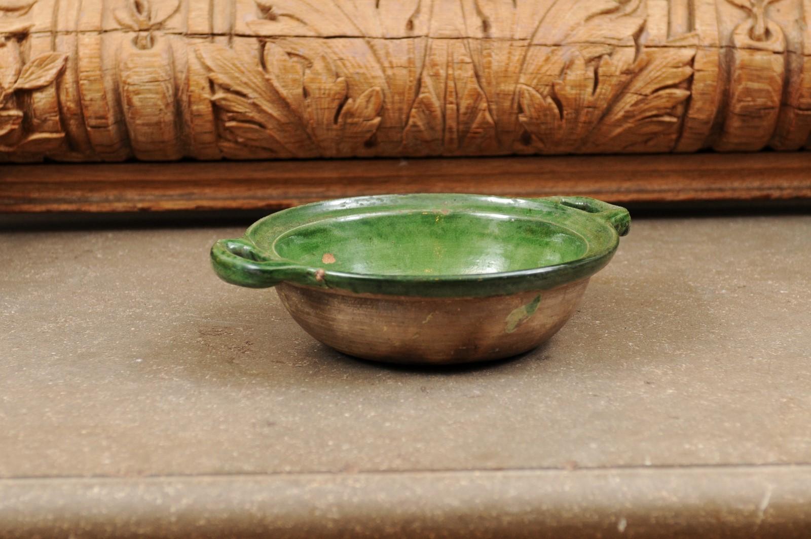 A French Provincial green glazed pottery bowl from the 19th century, with lateral handles and unfinished belly. Created in France during the 19th century, this pottery bowl features a circular body adorned with a green glaze on the interior, while