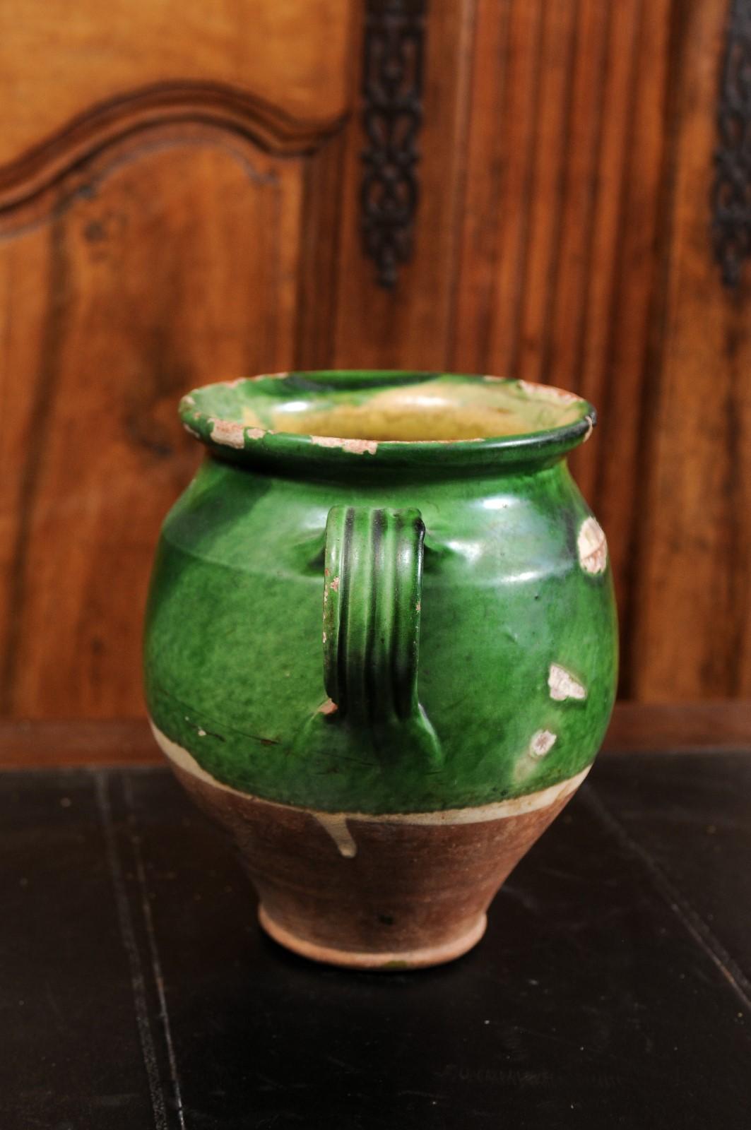 A French green glazed pottery confit pot from the 19th century with two handles and unglazed base. Created in France during the 19th century, this confit pot features a green glaze in its upper section sitting above an unfinished base. Traditionally