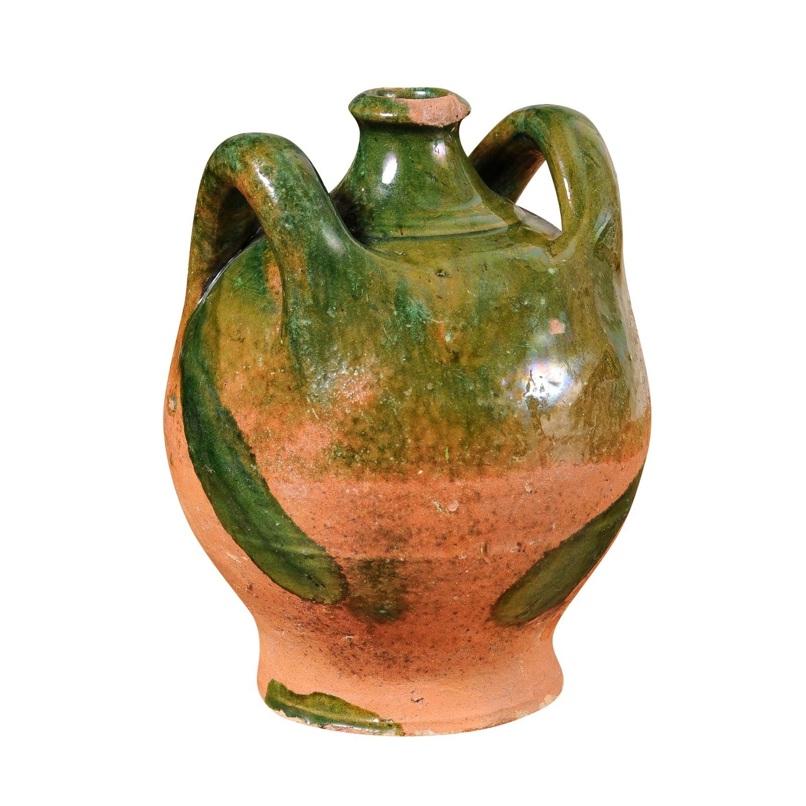 A French Provincial pottery jug from the 19th century with green glaze, dripping and lateral handles flanking the central spout. This 19th-century French Provincial pottery jug is a delightful embodiment of rustic charm and old-world craftsmanship.