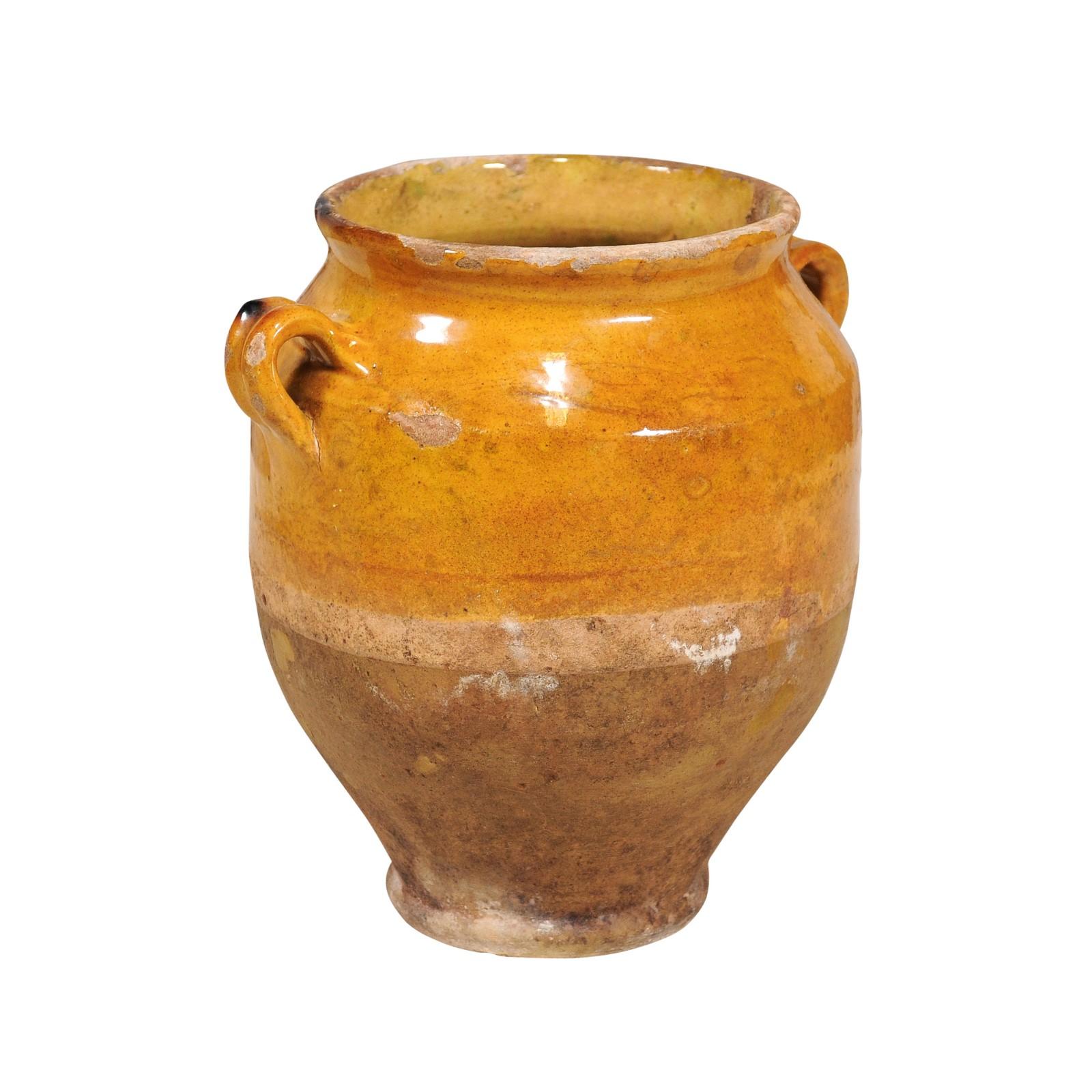 A French Provincial pot à confit pottery from the 19th century with yellow glaze and two handles. Immerse yourself in the rustic charm and warmth of this French Provincial pot à confit from the 19th century, a piece that embodies the essence of