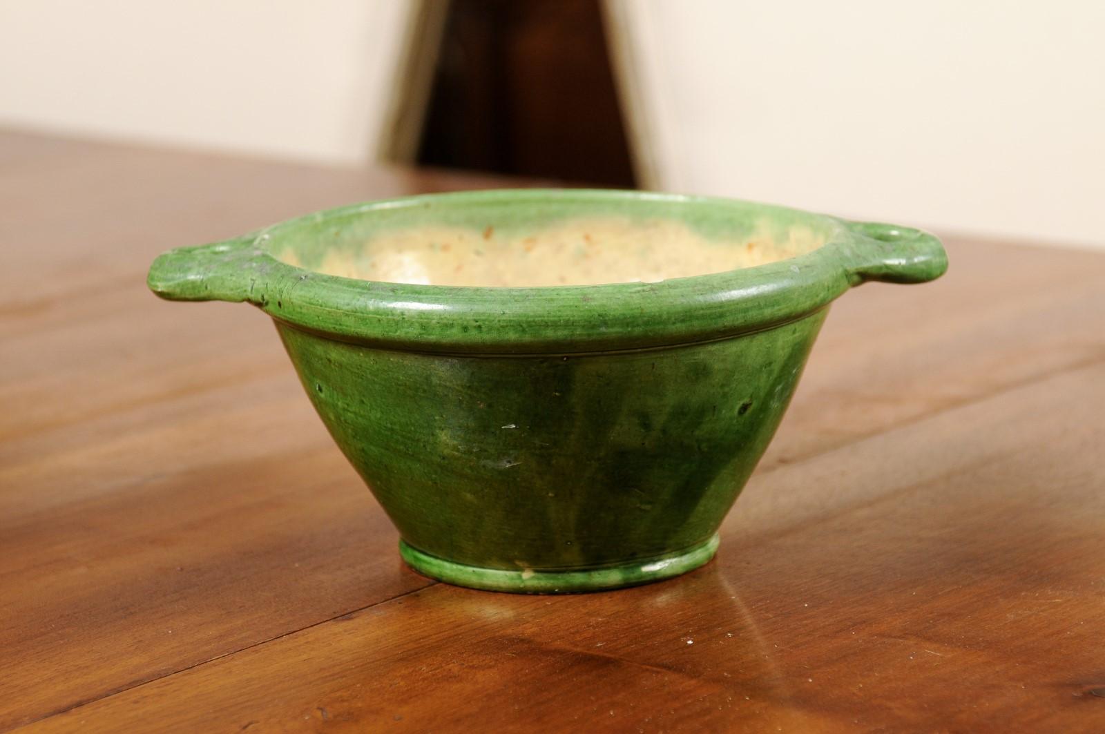 A French pottery bowl from the 19th century, with green glaze and side handles. Created in Southern France during the 19th century, this rustic bowl features a green glazed body with tapered lines, flanked with petite side handles. Boasting a nicely