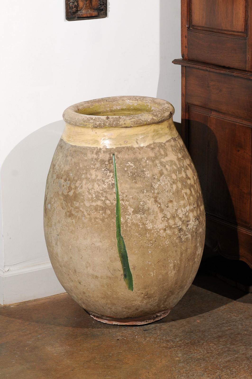 A French Provincial large size terracotta jar from Biot, Provence with yellow glaze and green drip from the 19th century. Created in Southern France during the 19th century, the olive jar features a recognizable round shape, showcasing yellow glaze