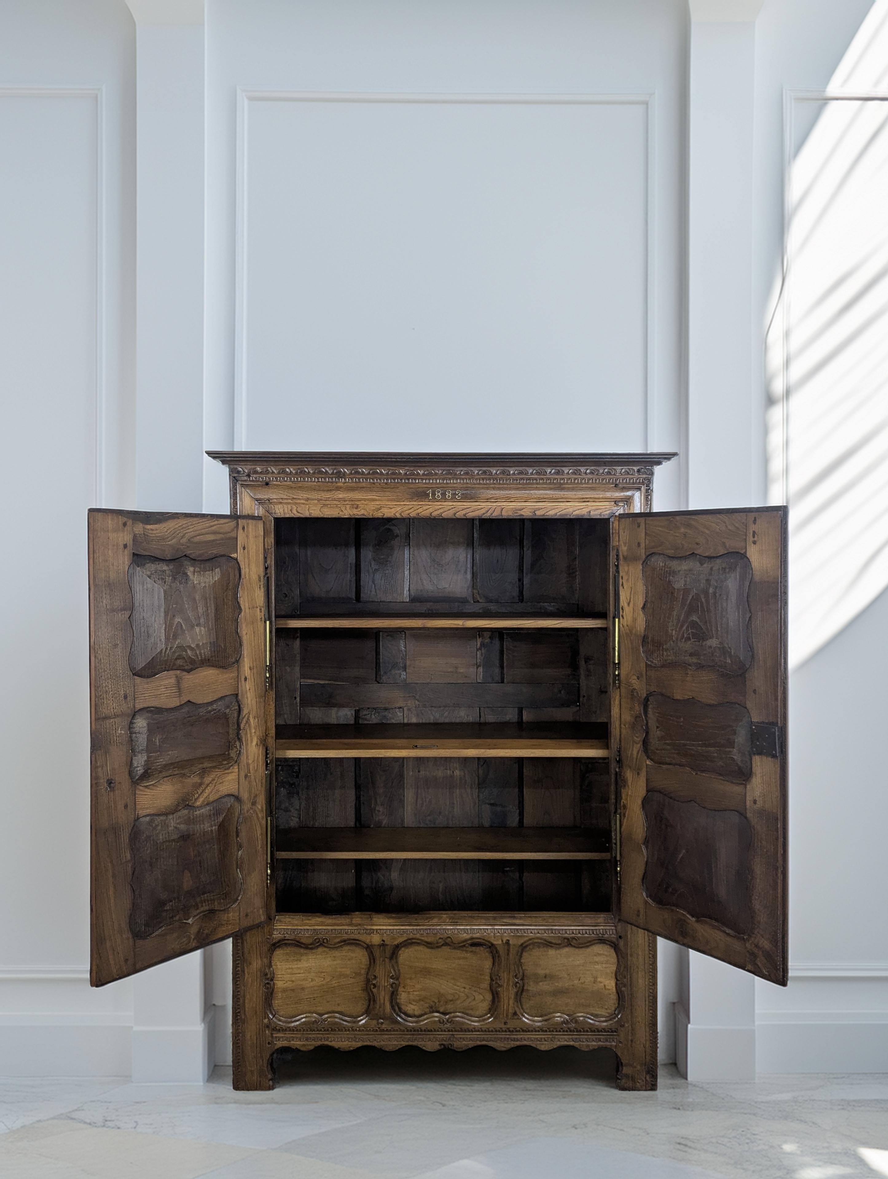 Questo armadio ricco di dettagli esemplifica l'eleganza dei mobili della Provincia Francese della fine del XIX secolo. Realizzato in noce massiccio, il pezzo presenta pannelli intagliati a mano con modanature a serpentina, rosette floreali e un