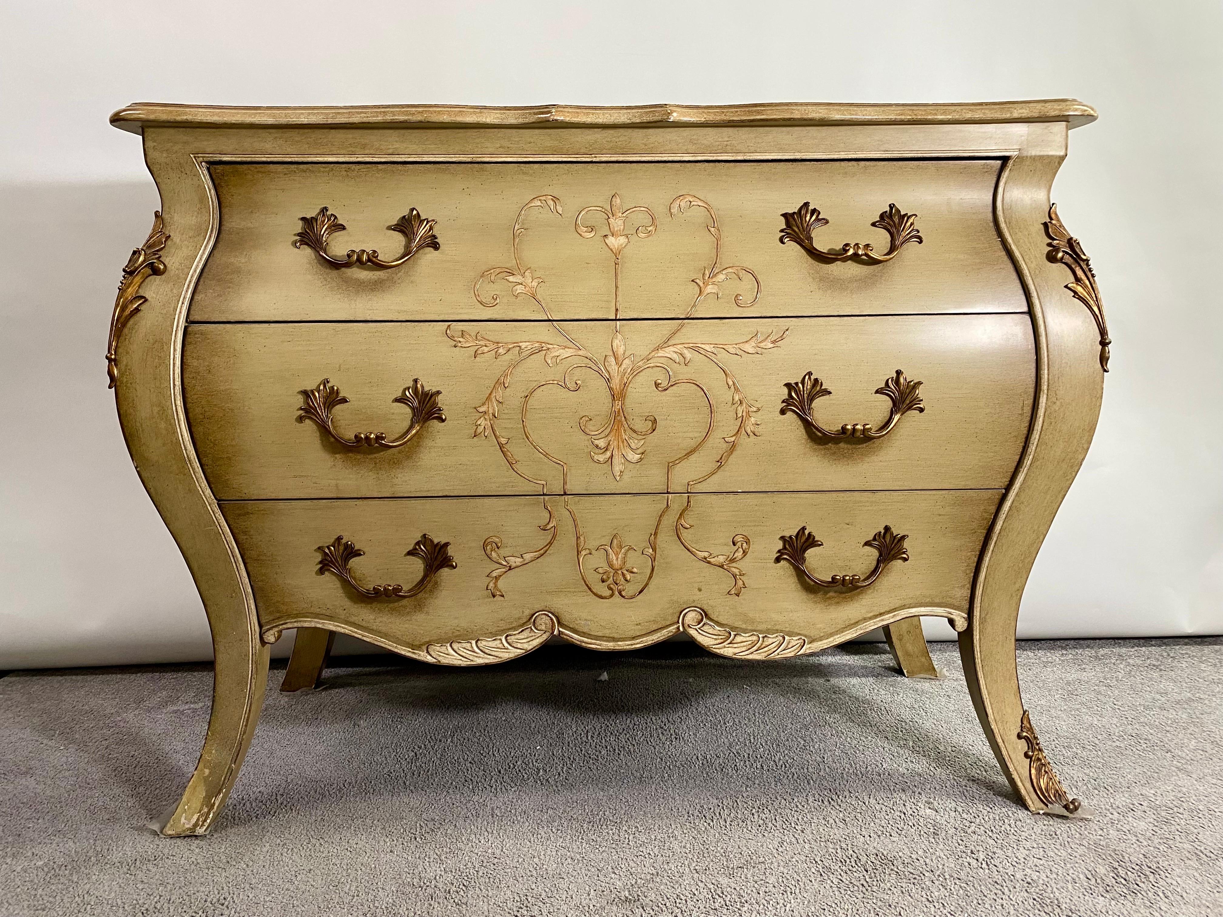A charming Drexel for Lilian August French Provincial bombe style chest or commode. The commode is beautifully hand-painted over beige antiqued color and features three drawers. The chest is finely decorated with cast bronze mounts on the side and