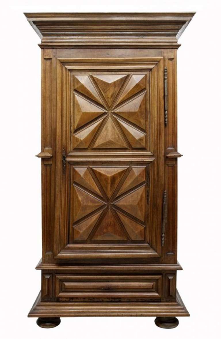 18th century French Provincial Bonnetiere, likely Brittany, a stepped crown over a single door with large exposed hinges, a lower drawer, raised on with a wide stepped base, the front and side with raised geometric panels.