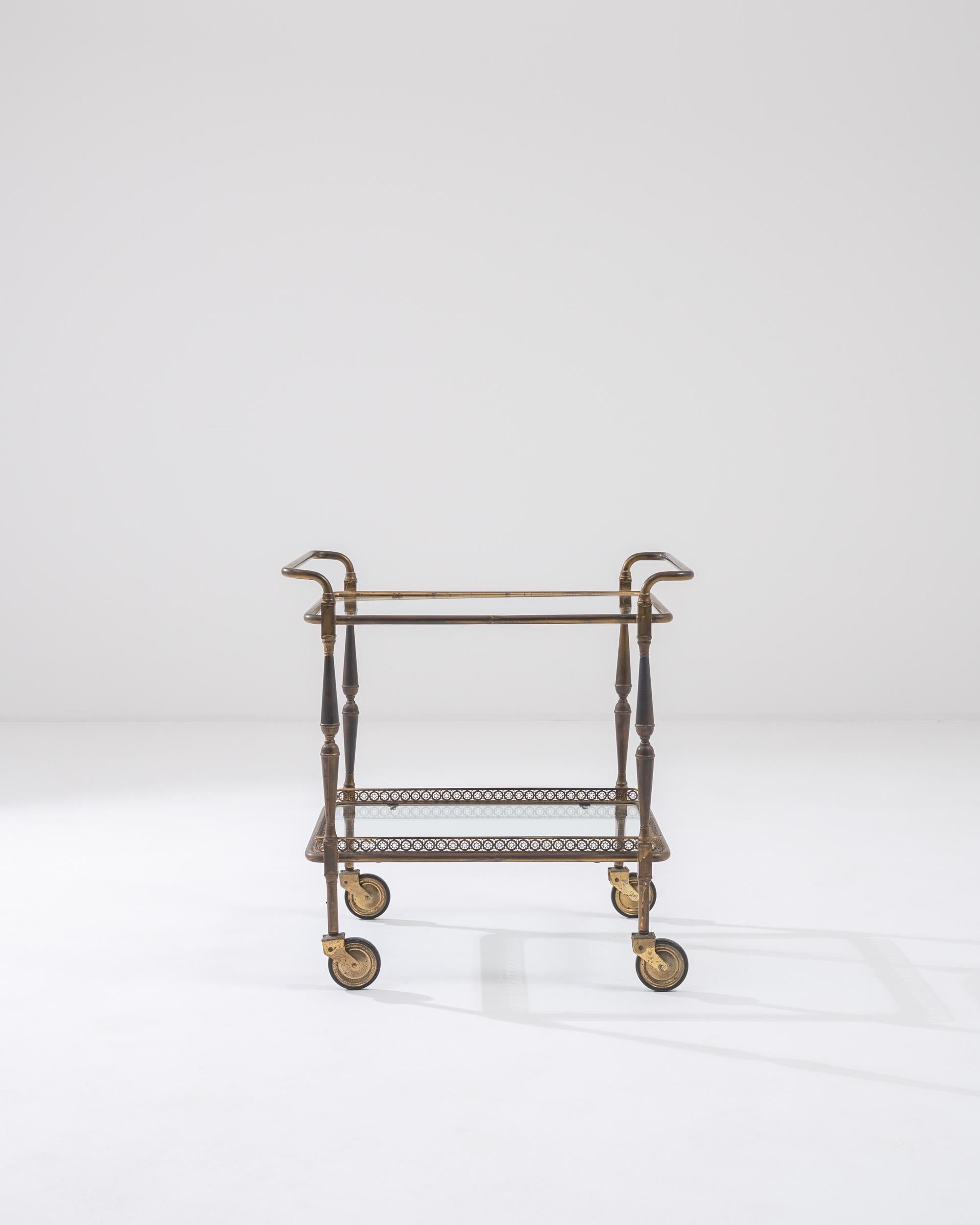 A metal bar cart created in 20th century France. With tastefully rounded brass tubes and sumptuously spindled legs, this speedy little bar cart offers both a practical and playful companion. Through its age and experience, a light and eye-pleasing