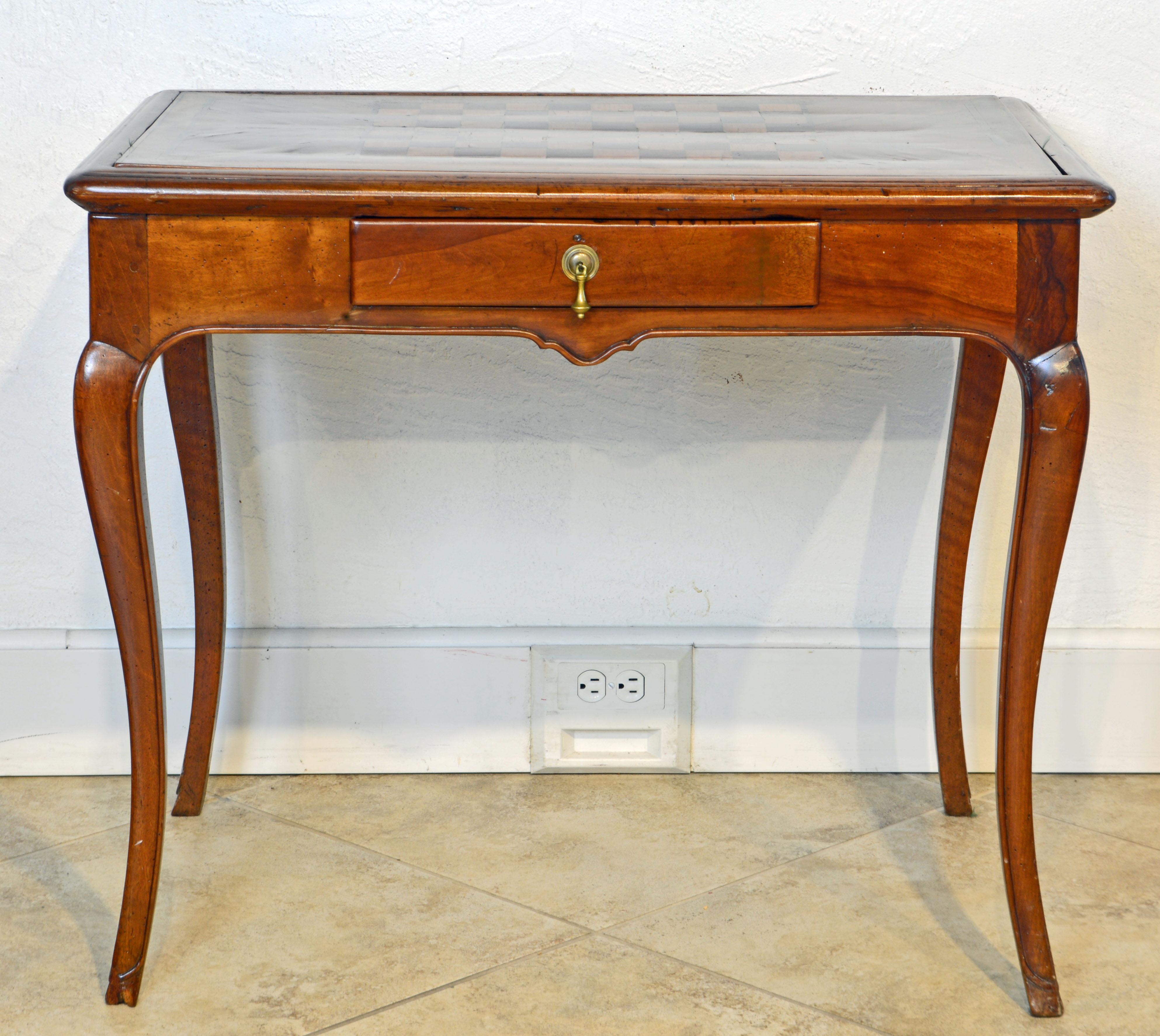 This early 19th century French Provincial fruitwood one drawer chess and game table features a kingwood, tulipwood and mahogany parquetry top which can be turned over revealing a surface lined with green fabric for playing cards. The aprons are