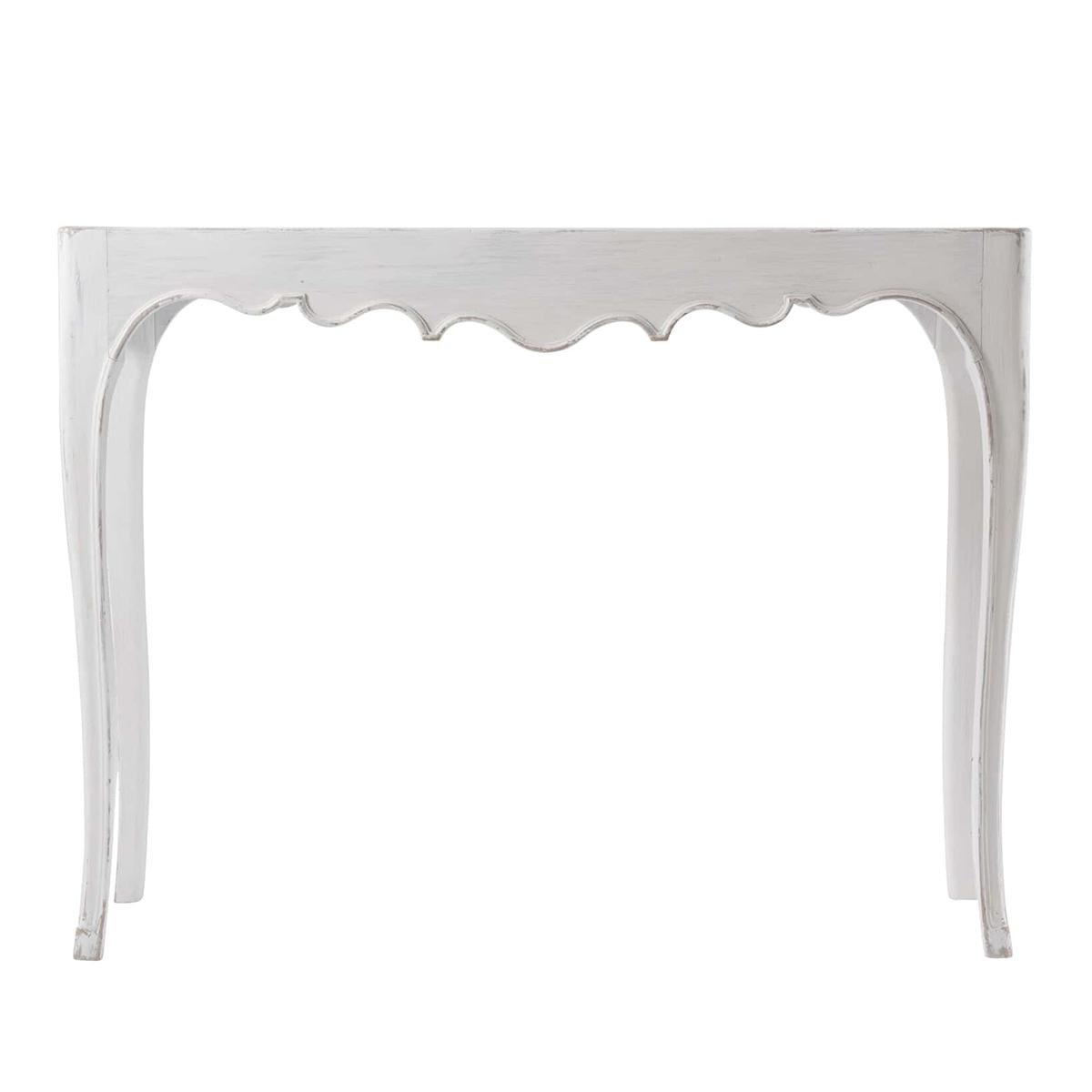 A French Provincial console table with a distressed white painted finish, a molded dish top, a carved scalloped apron on carved and molded cabriole legs.
Dimensions: 42.5