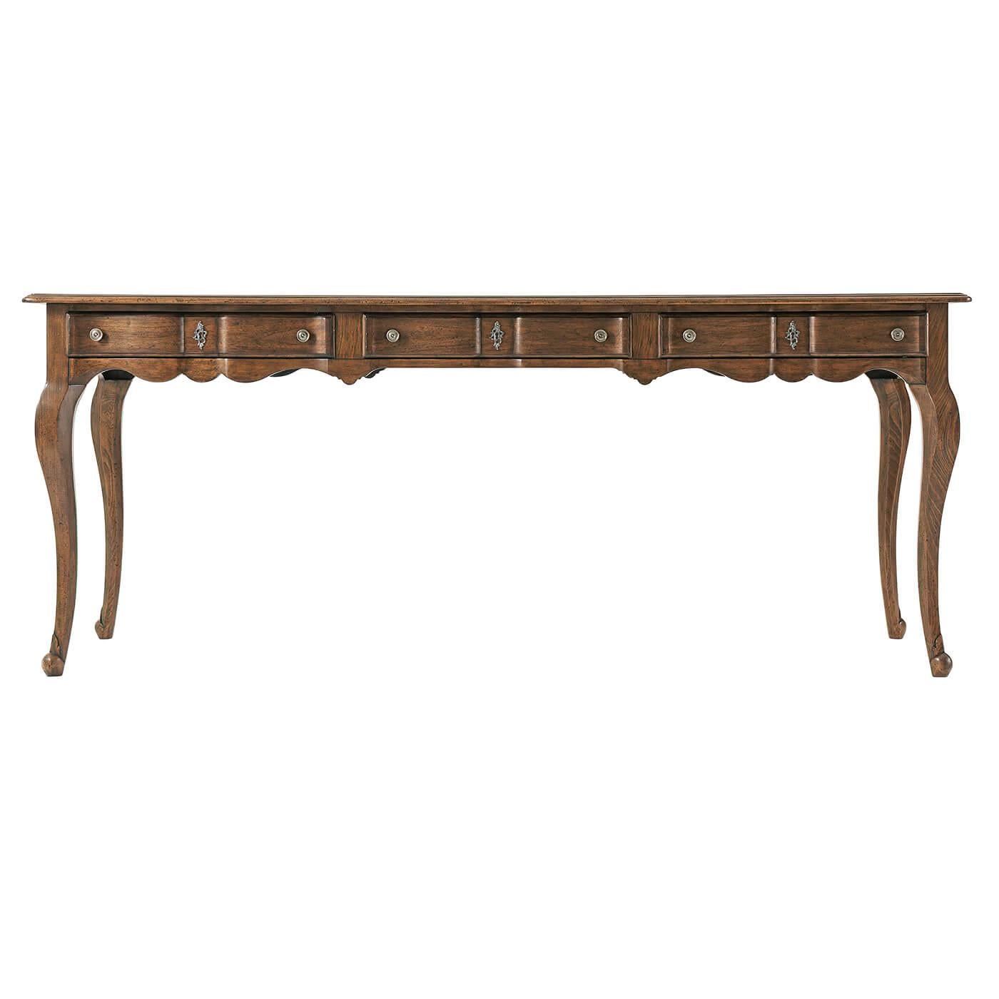 French Provincial carved beach and walnut bureau plat or writing table with a slightly antiqued and distressed finish, serpentine molded edge top, three molded edge serpentine front drawers with scalloped frieze, brass handles and escutcheons on