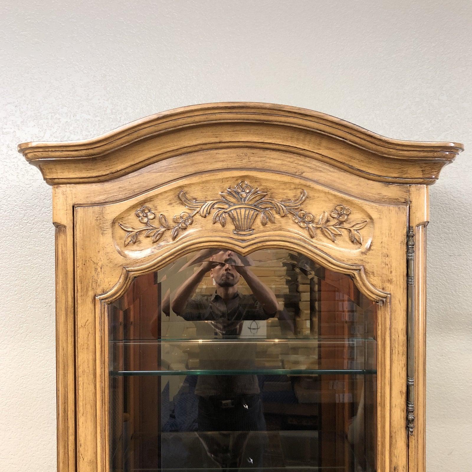 A French Provincial styled Curio cabinet. The antiqued finish highlights the traditional curves and carvings. Arched glass windows allow viewing from front and sides, the lighting from above flows all the way through the adjustable glass