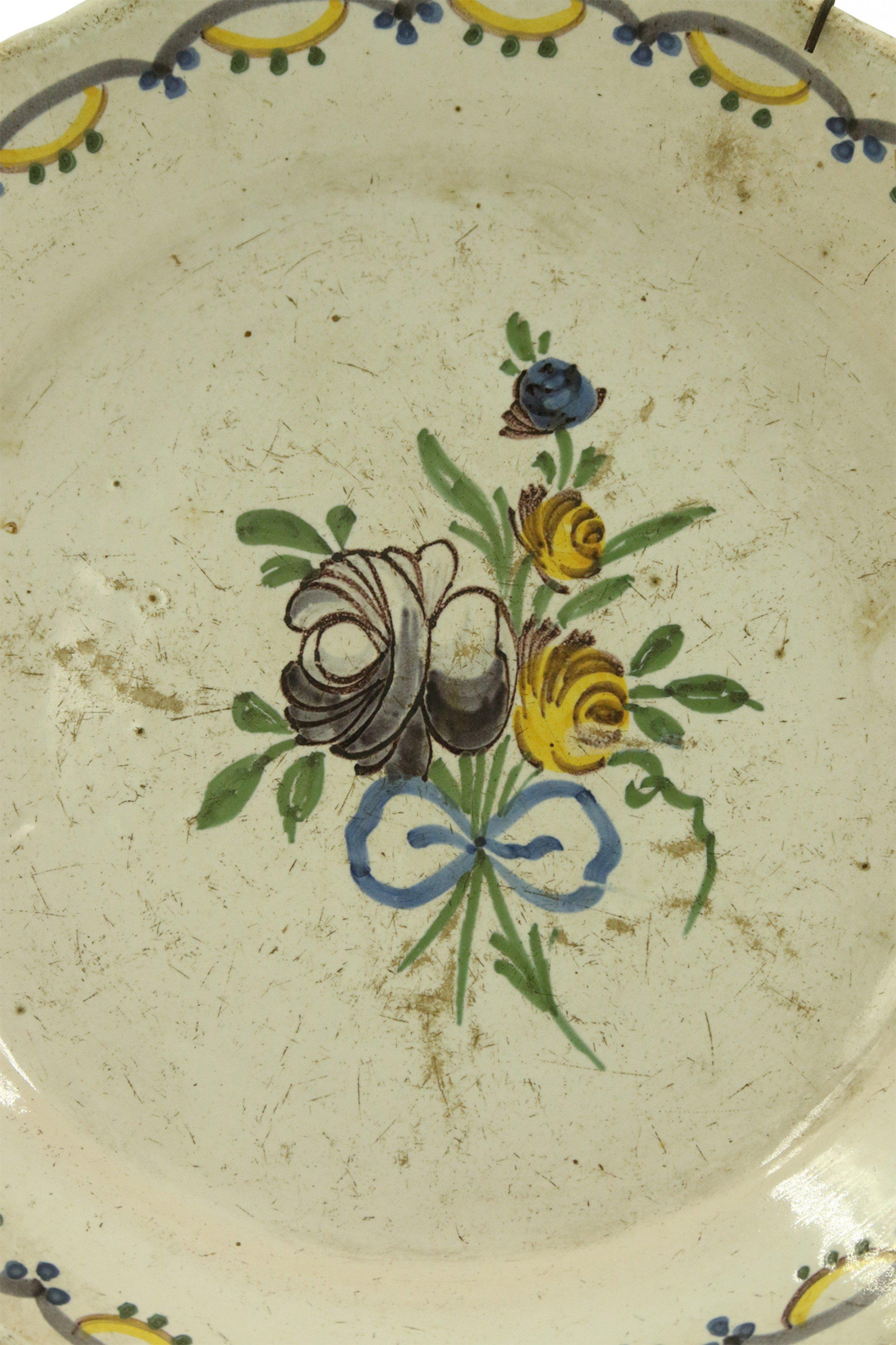 Assiette en faïence de Nevers (XVIIIe siècle), de style provincial français, avec au centre une gerbe de fleurs et un bord festonné avec une bordure peinte à la main en bleu et jaune.
    