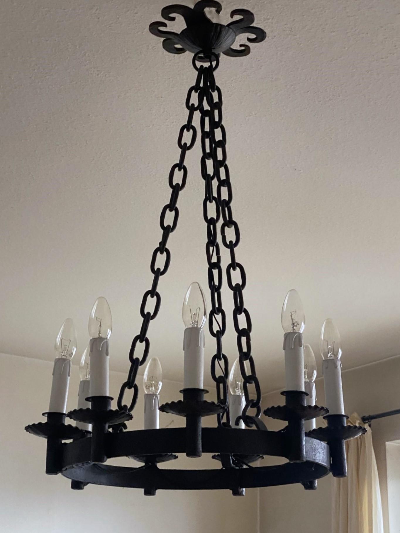 Very elegant Spanish Colonial, French Country style nine-light handelier, France, circa 1920-1930. Large rustic hand-forged ring supporting nine candelabra lights, suspended by three iron chains conecting to a large iron ceilinling rosette.
In very