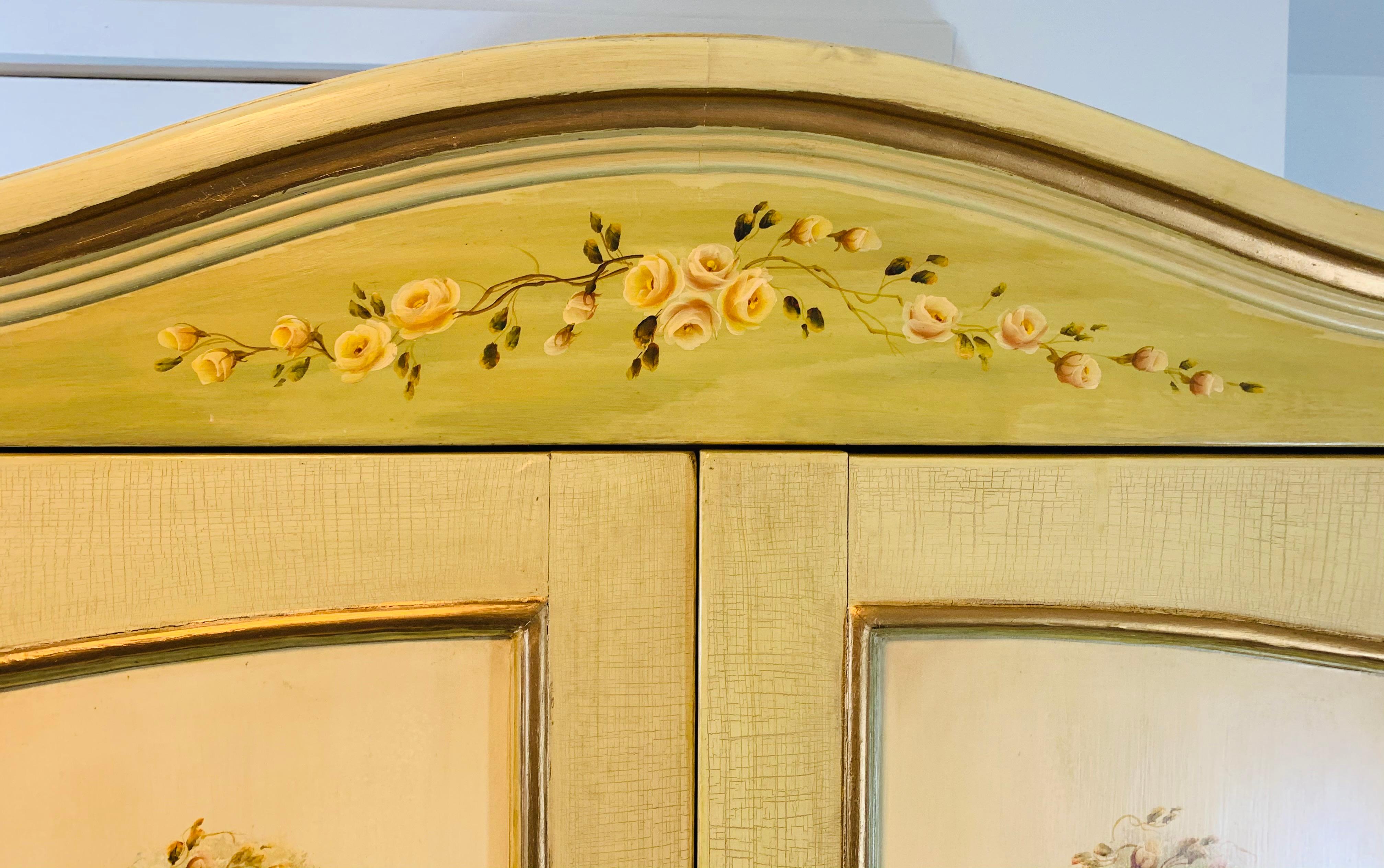 A stunning French Provincial armoire romantically hand painted in antiqued cream and light green colors with large plant design on each door and exquisite floral pattern on the drawers and the sides. The two door armoire features storage space