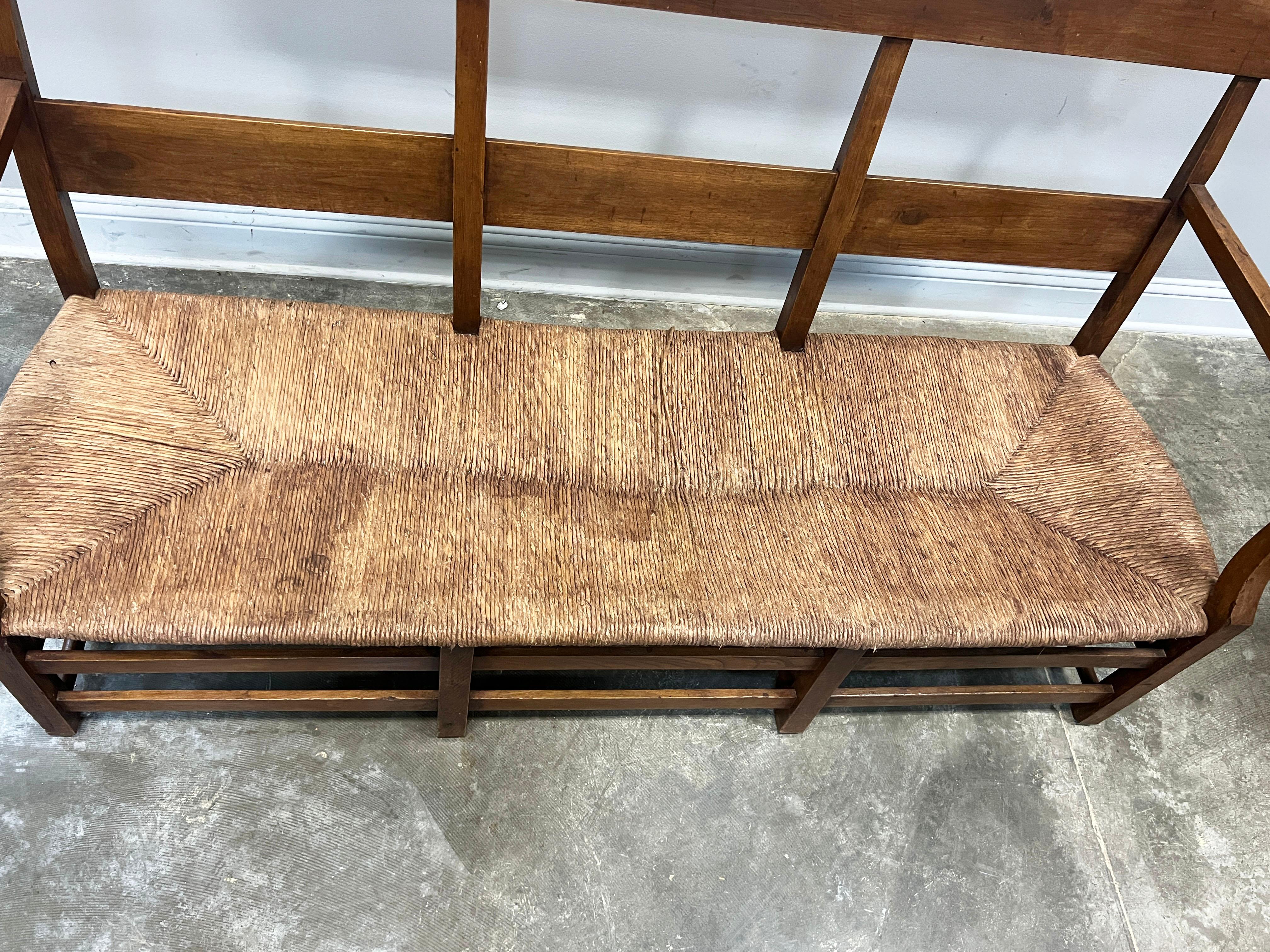 19th century banquette in cherry, warm beautiful patina consistent with its age. Pegged joints and rush seat in good antique condition.