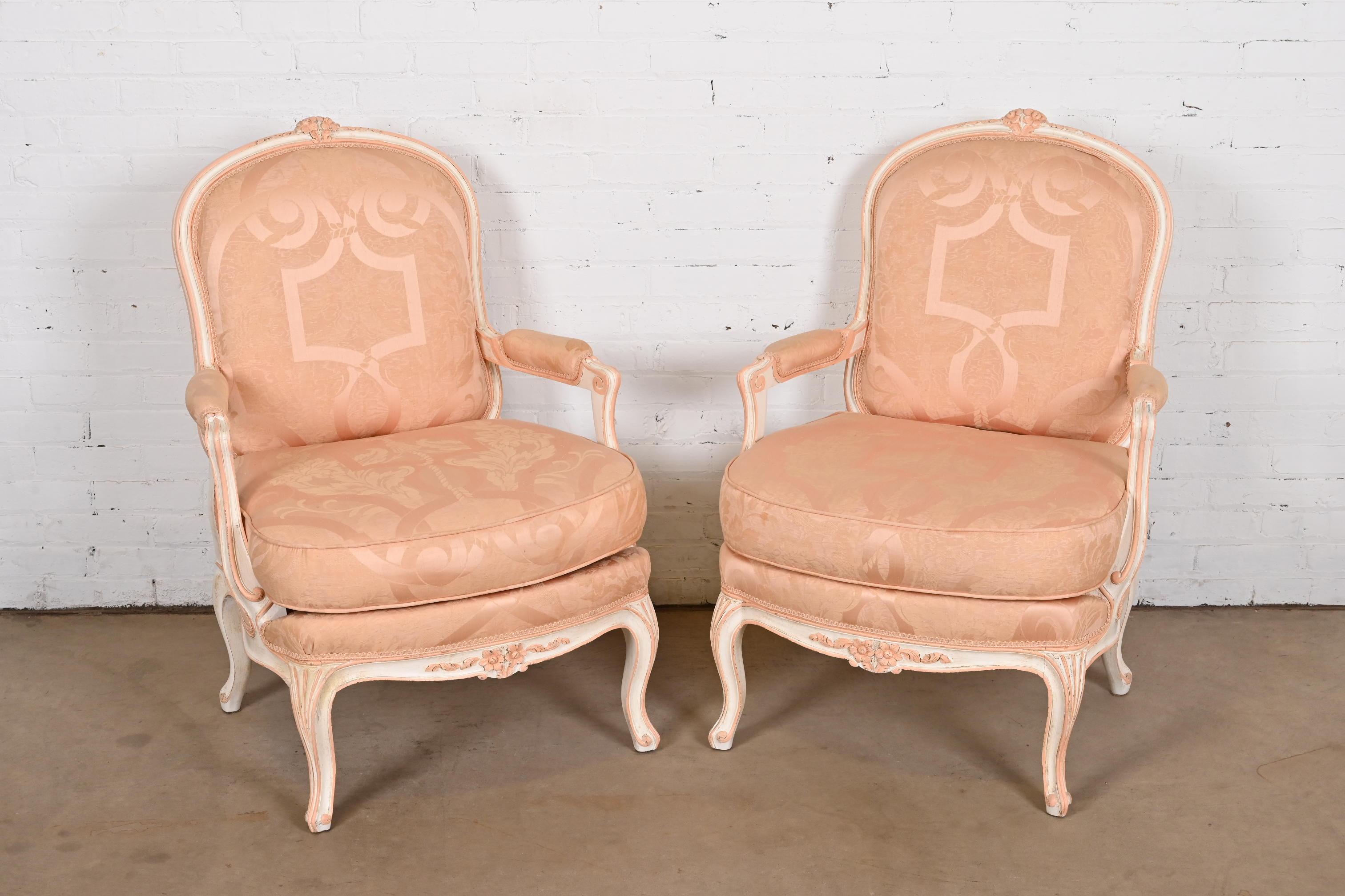 A gorgeous pair of French Provincial Louis XV style upholstered lounge chairs or Bergere chairs

In the manner of Baker Furniture

USA, Circa 1940s

Carved walnut frames, painted in cream and light pink with pink damask upholstered seats and