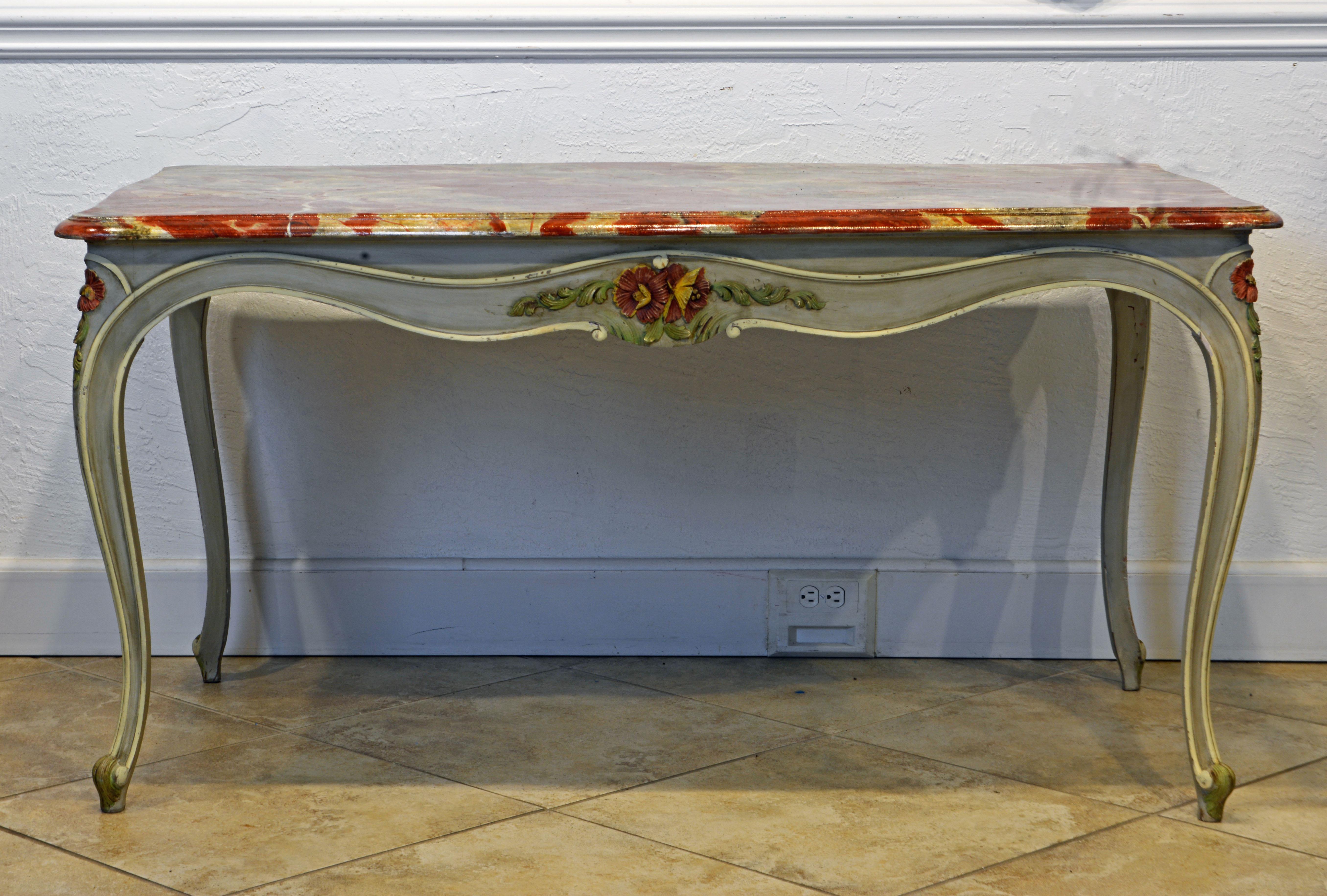 This vintage French Provincial painted dining table in the Louis XV style features a boldly marbleized top above curved aprons centering decorative multi color carved flowers and leaf work on all four sides. The curved aprons continue graciously to