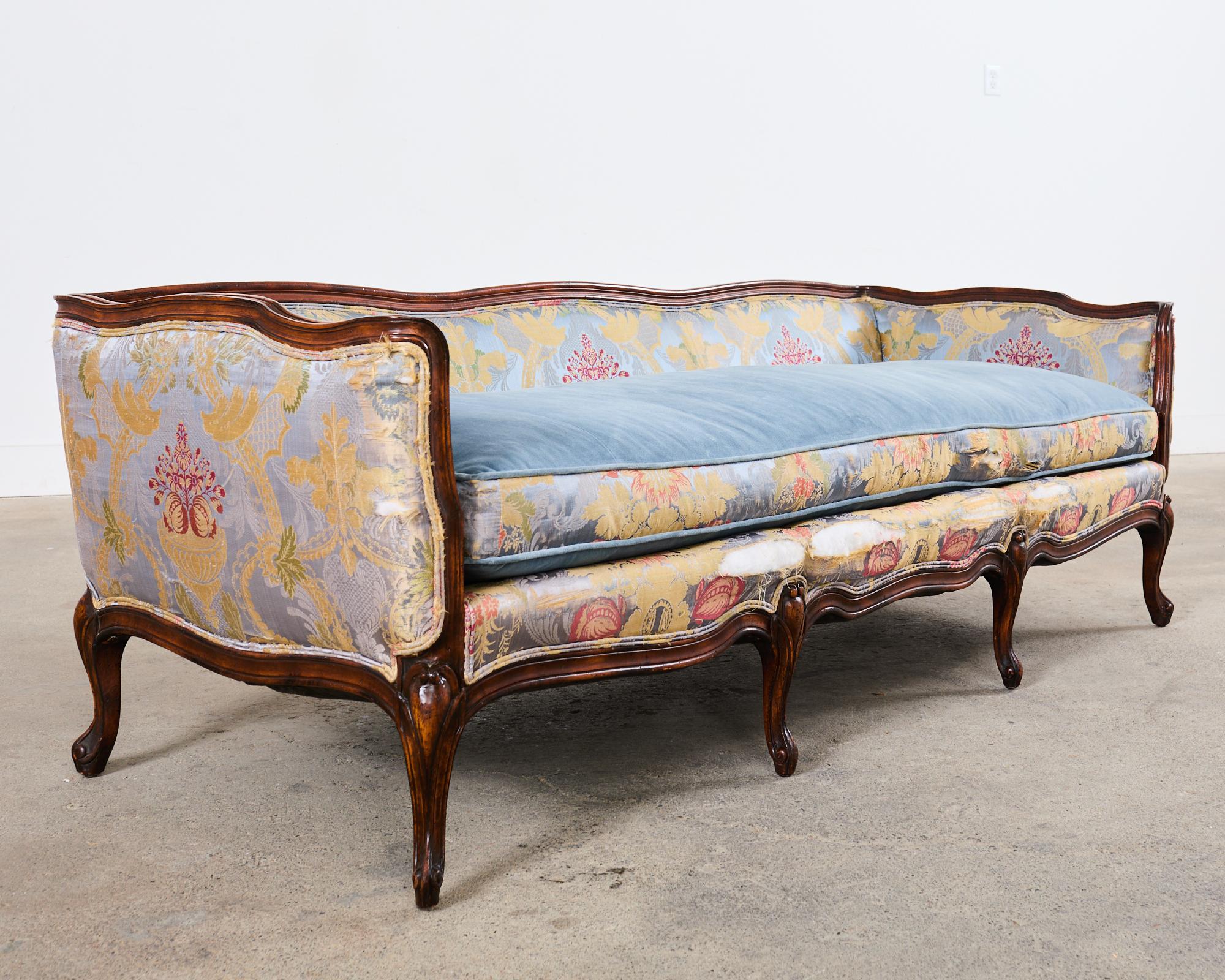 Gorgeous country French provincial canape sofa or settee made in the Louis XV taste. The sofa features a beechwood low profile carved frame with a serpentine back, arms, and apron. The settee has vintage upholstery fabric that is worn with losses