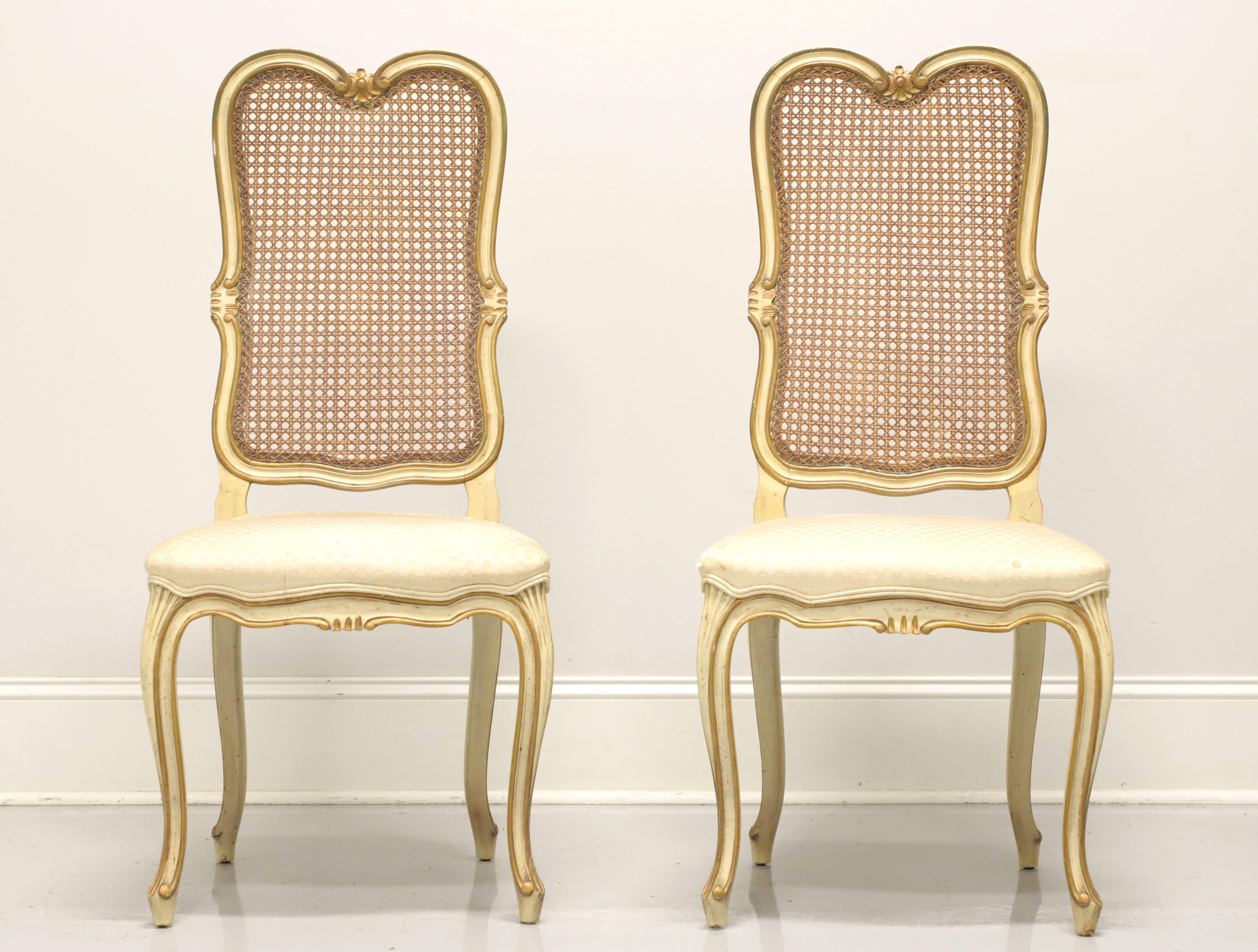 A pair of vintage French Provincial Louis XV style dining side chairs, unbranded, possibly by Davis Cabinet Co. Cherry wood painted an antique white with gold accents, cane backs, fabric upholstered seats, curved legs and scroll feet. Made in the