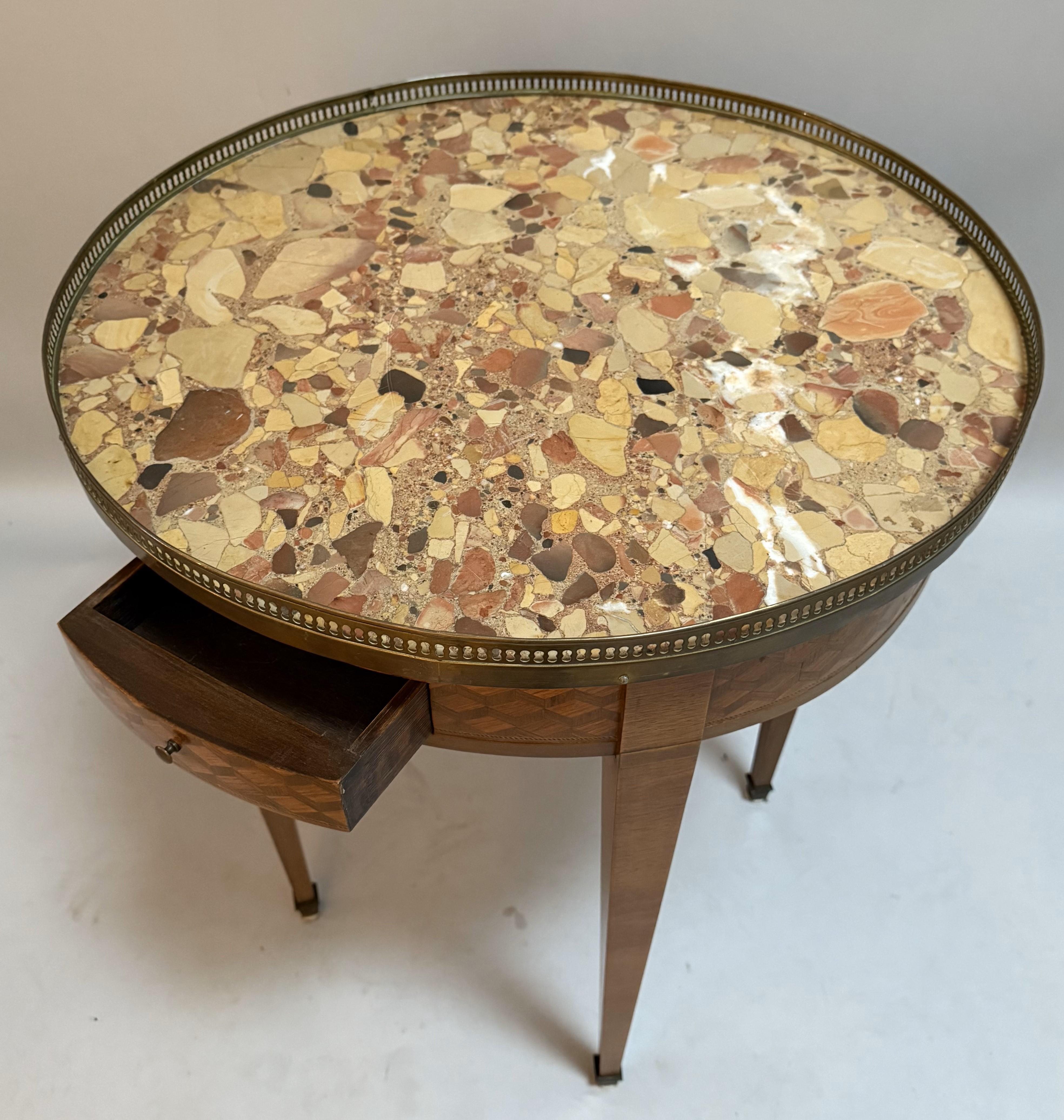Exquisita mesa auxiliar de estilo Luis XVI francés, fabricada en el norte de Francia hacia 1840. Esta elegante mesa circular presenta un inconfundible tablero de mármol espécimen en vibrantes tonos terrosos, enmarcado por una galería de bronce