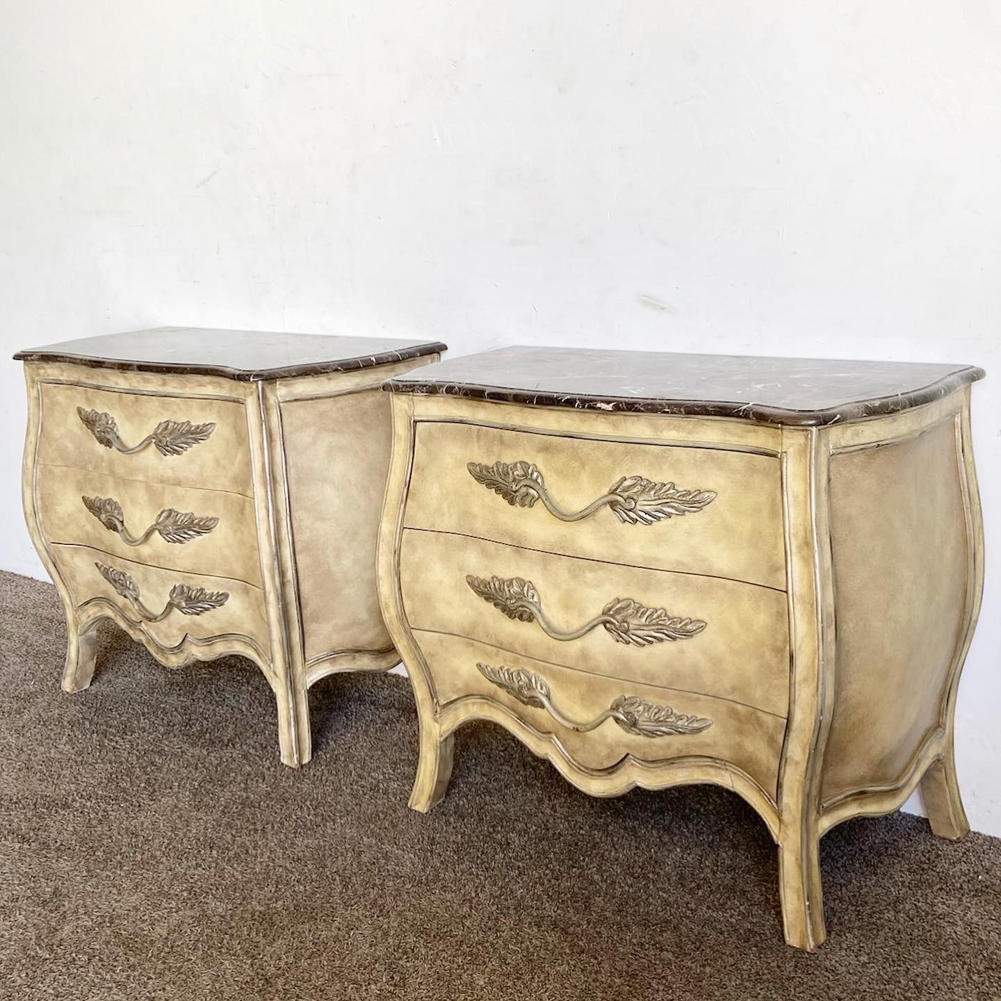 Experience classic French elegance with this pair of Marble Bomb√© Commodes. Their distinctive bulging silhouette, a hallmark of the Bomb√© style, is beautifully crowned with luxurious marble tops. Adorned with intricate detailing, these wooden