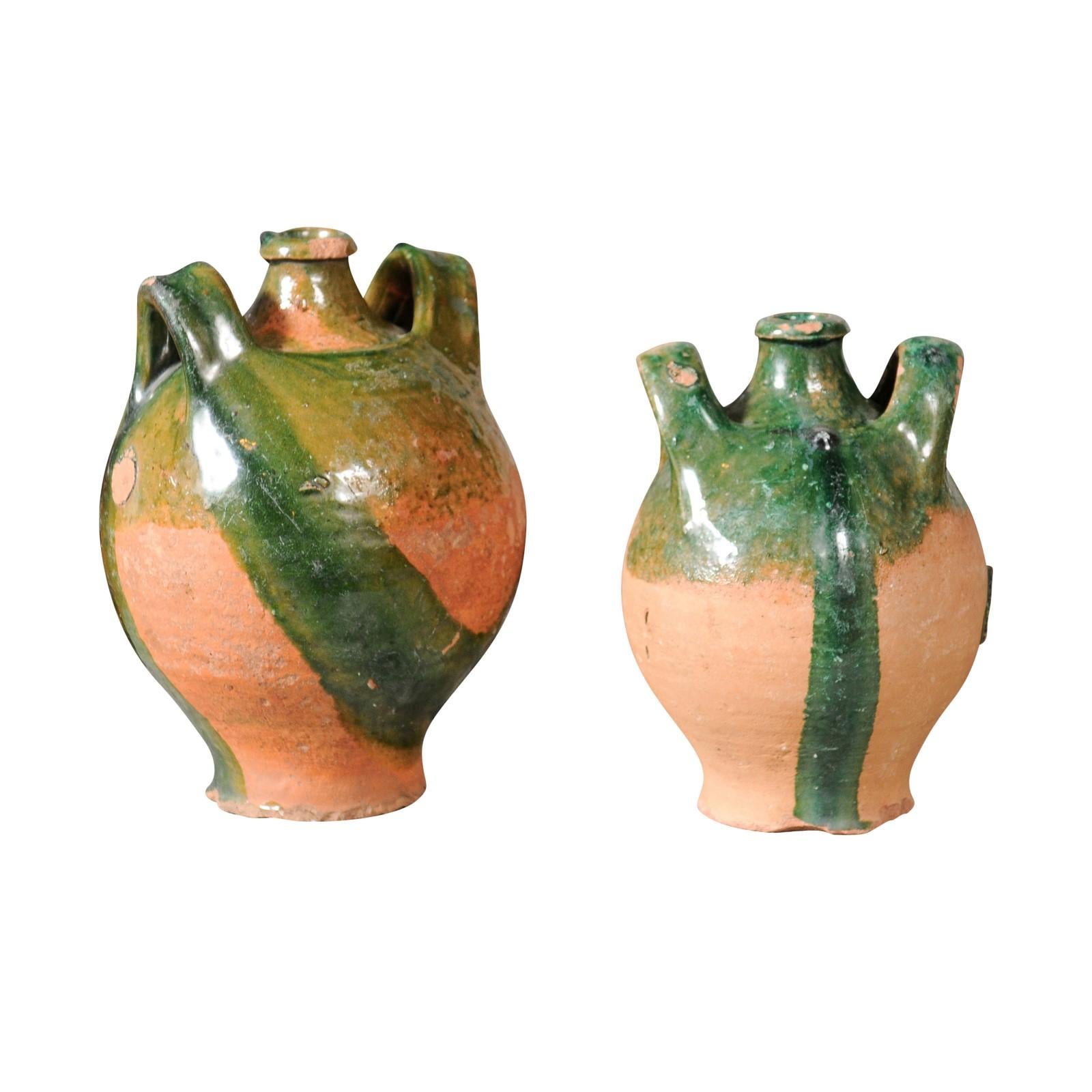 Deux pichets en poterie provinciale française de l'époque Napoléon III, vers 1850, avec glaçure verte, goutte à goutte et poignées latérales flanquant le bec verseur central. Ils sont vendus à l'unité. Paire de cruches en poterie d'époque Napoléon