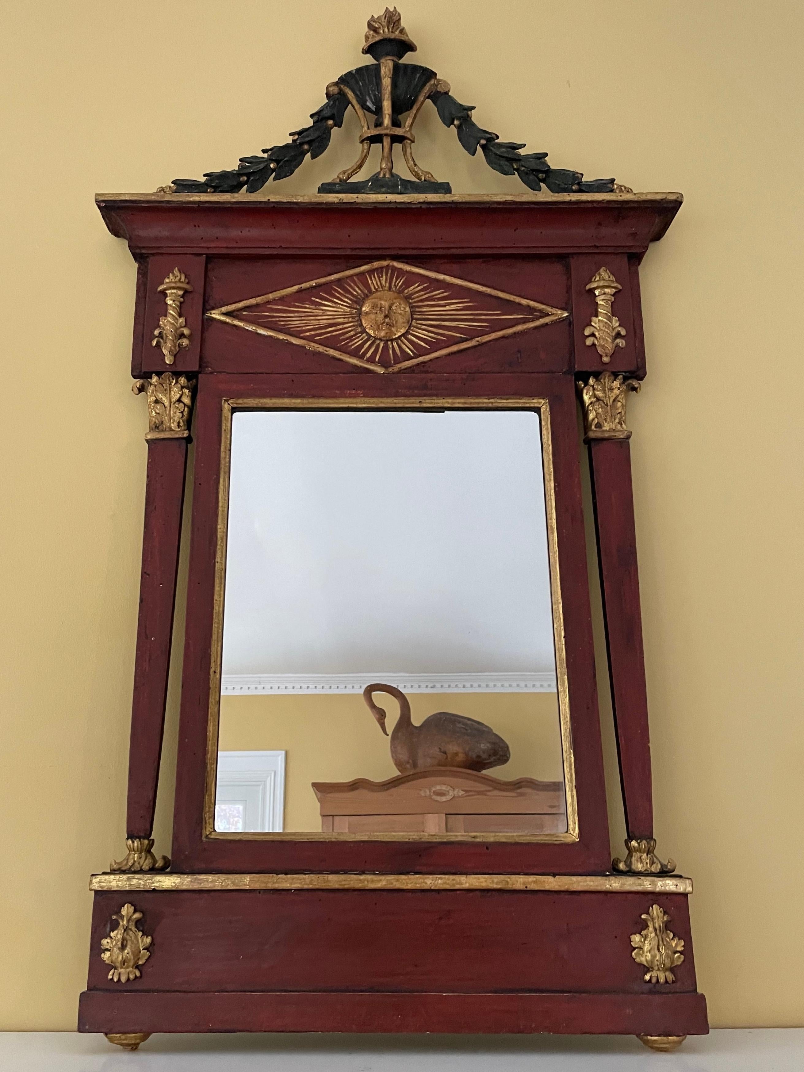 French provincial neoclassical mirror. Red, green and gilt painted neoclassical style tabernacle form mirror with central plate flanked by tapering pilasters with flambeau block above centering a gilt rayed sun all beneath a flaming gilt torchiere