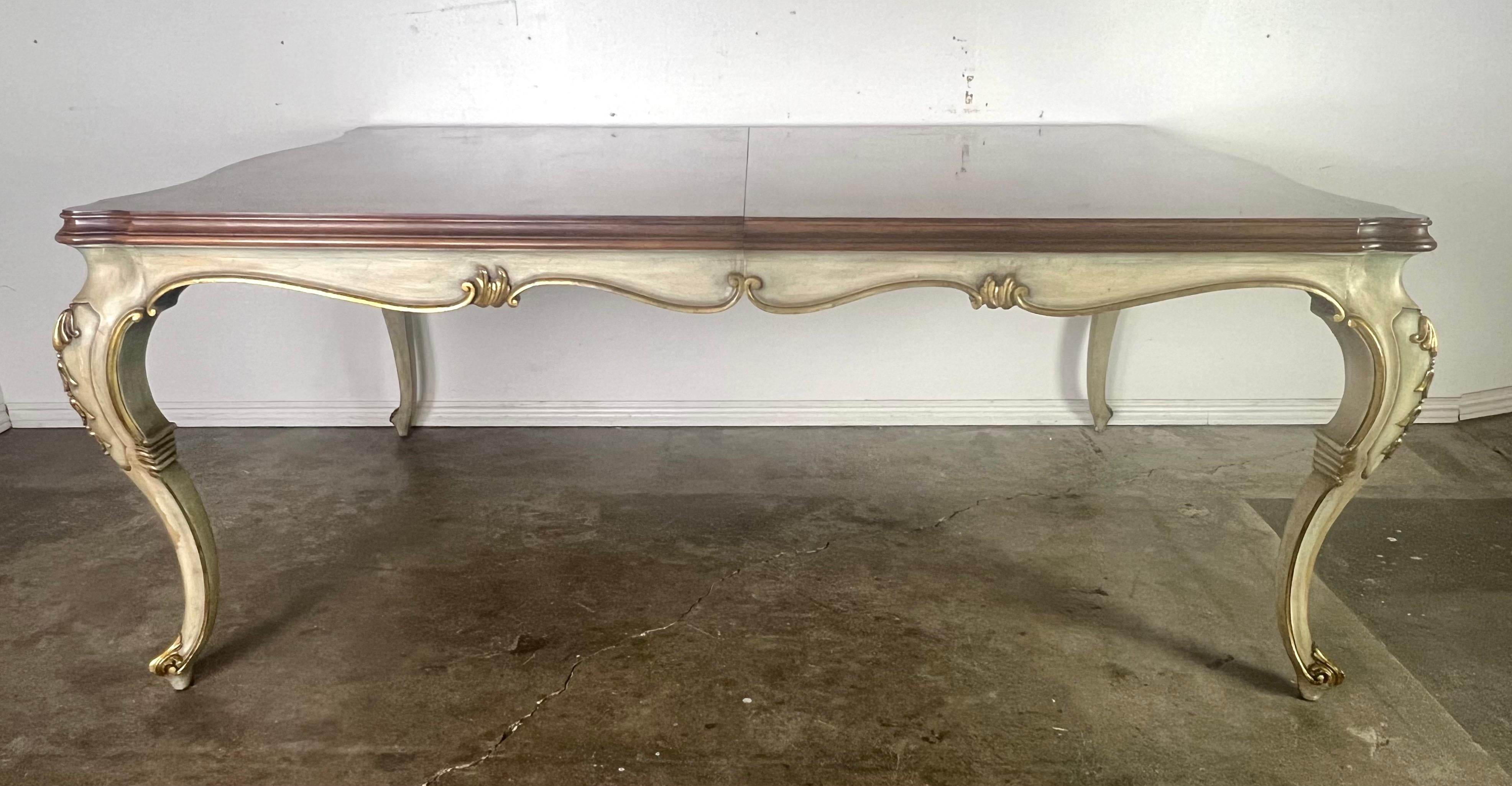 Table de salle à manger peinte de style provincial français avec un plateau incrusté.  La table repose sur quatre pieds cabriole avec un élément décoratif orné près du haut des pieds.  La table présente des sculptures et des détails décoratifs