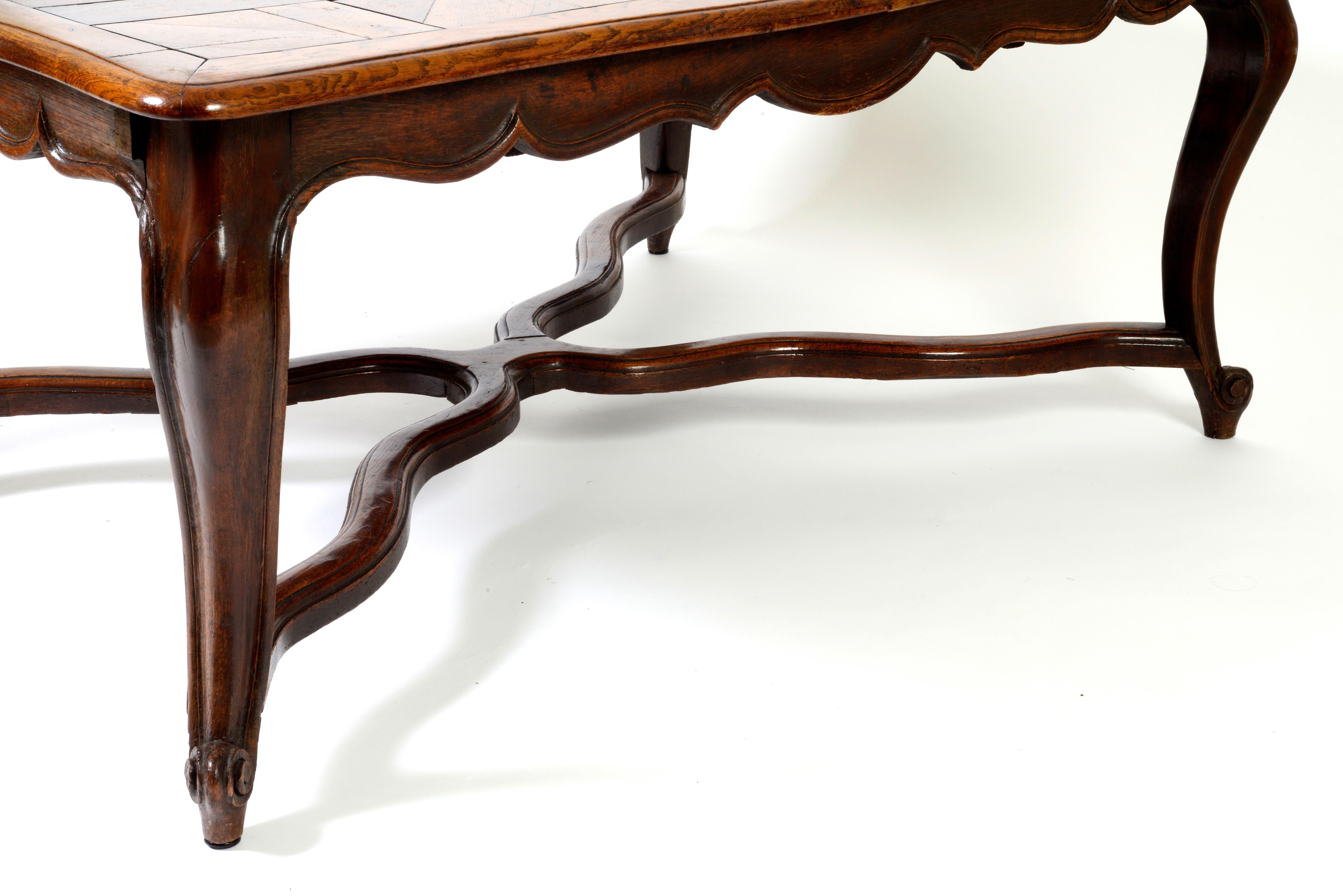 Provincial oak parquetry extending dining table with later base. The 18th century top separates and supports a large parquetry drop-in leaf. The base has a scalloped apron, curving 